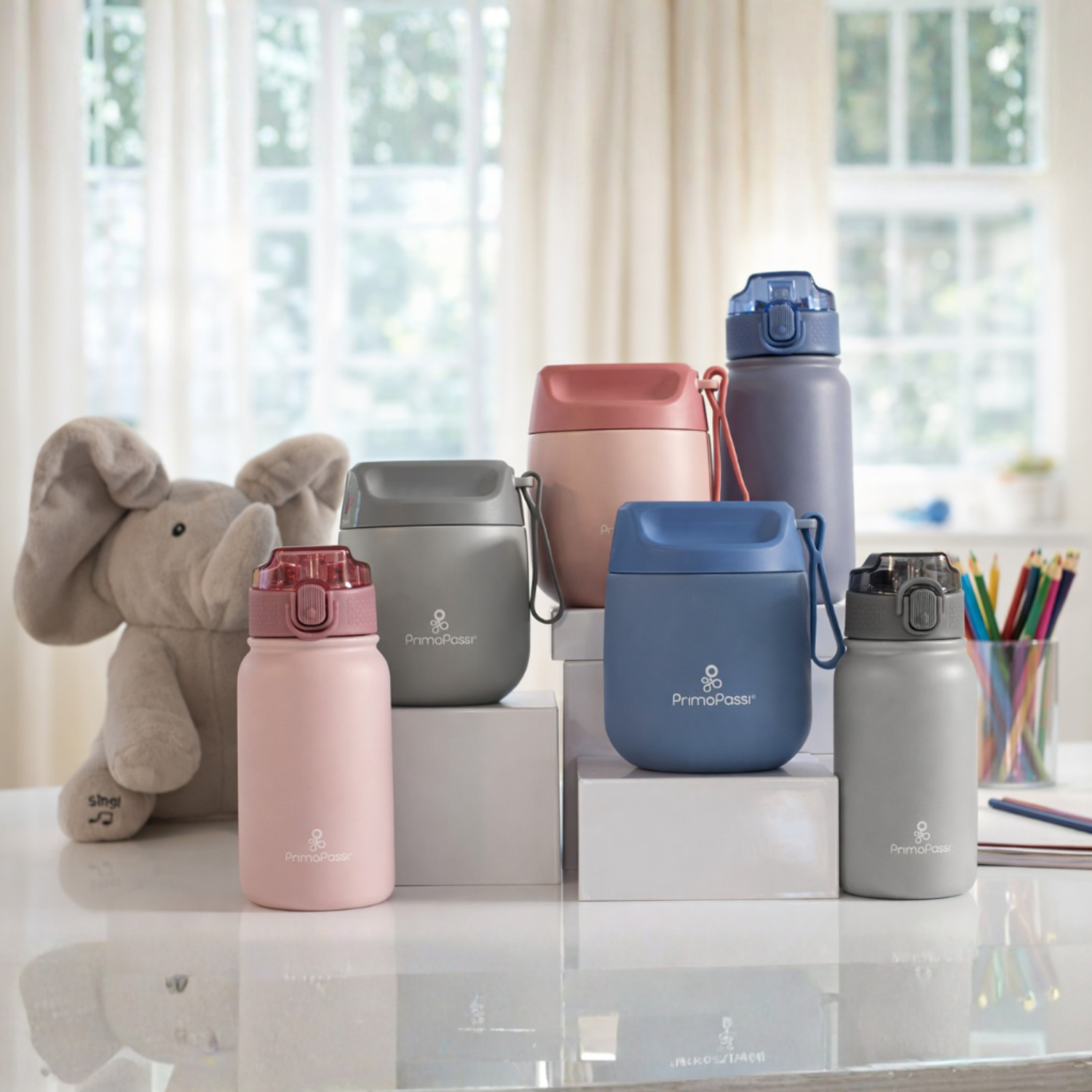 Collection of colorful insulated water bottles or food jars on a desk with a plush elephant toy and office supplies.