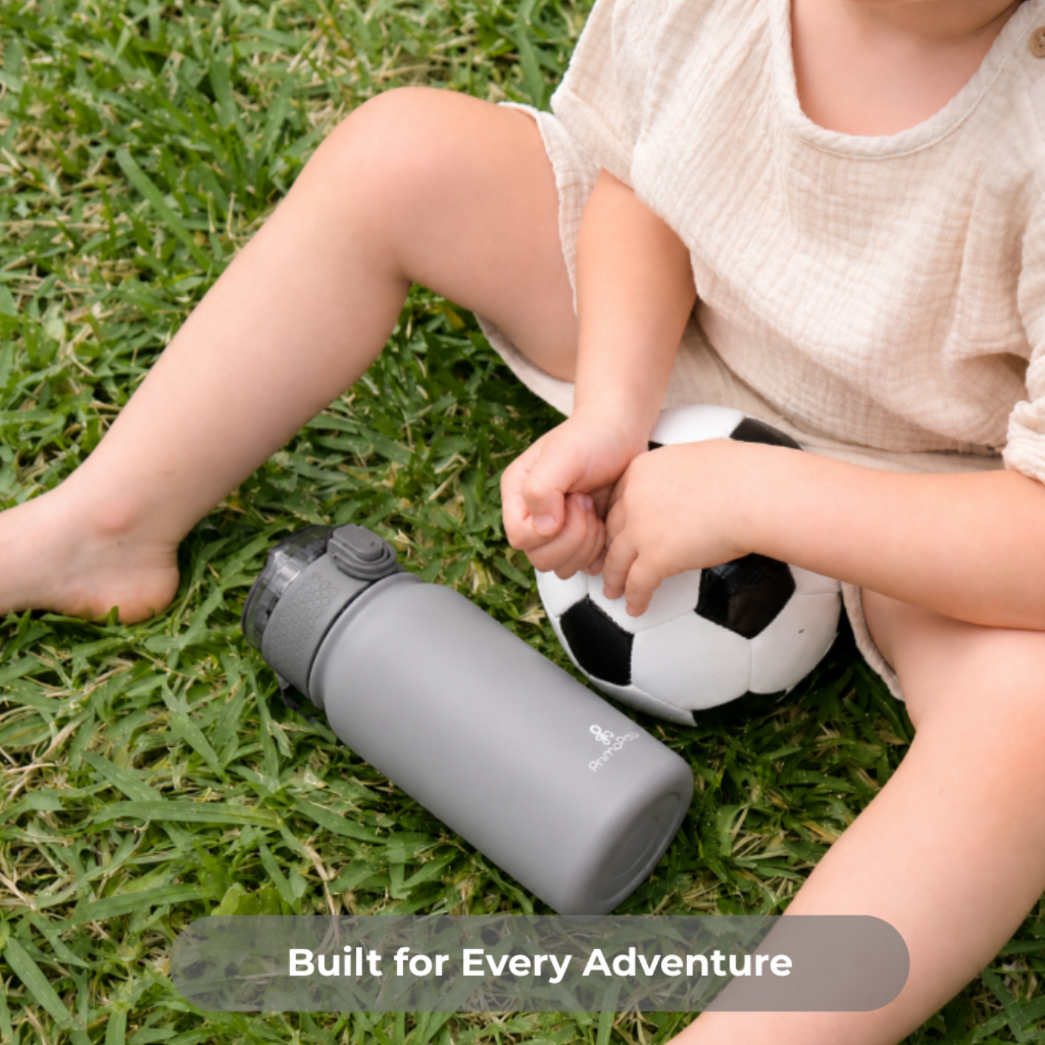 Child sitting on grass with a soccer ball and gray water bottle, text 'Built for Every Adventure'.