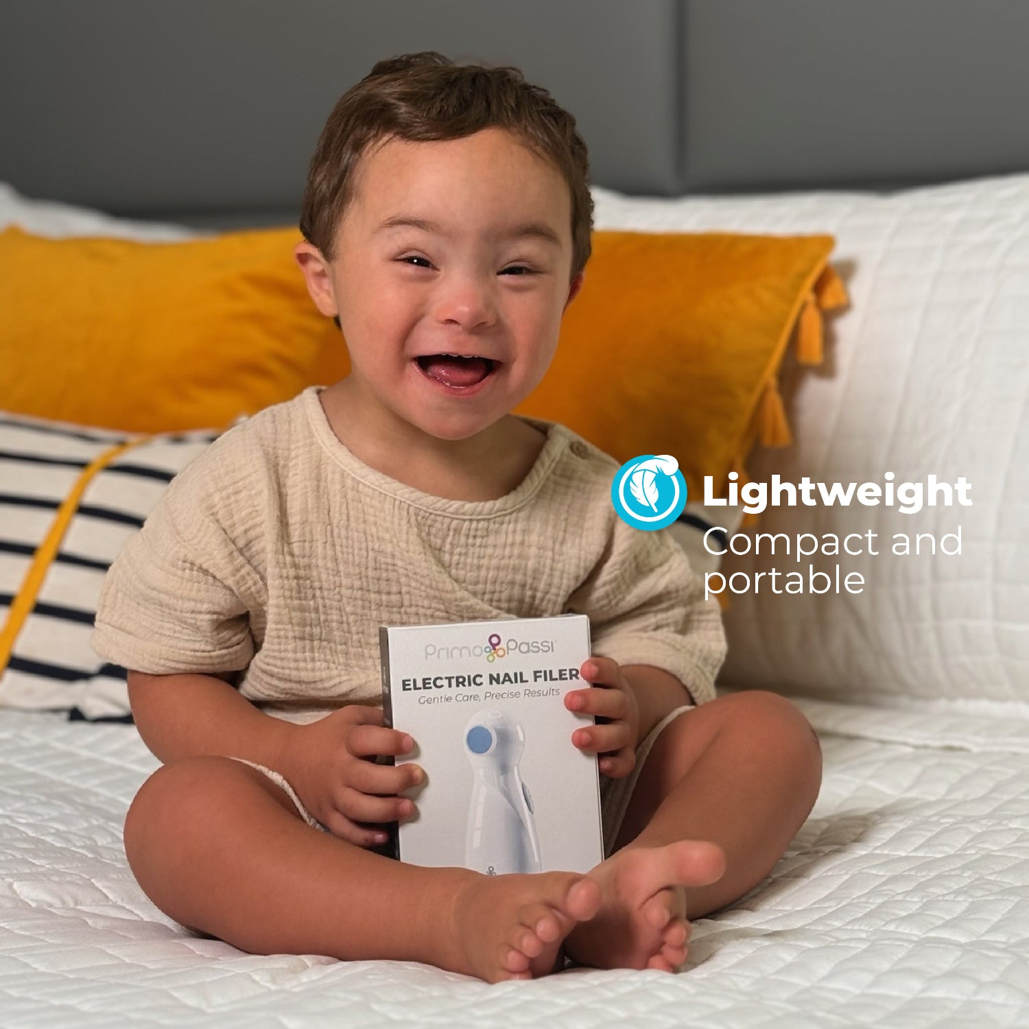 A baby smiling holding the box of white electric nail filer on a bed background