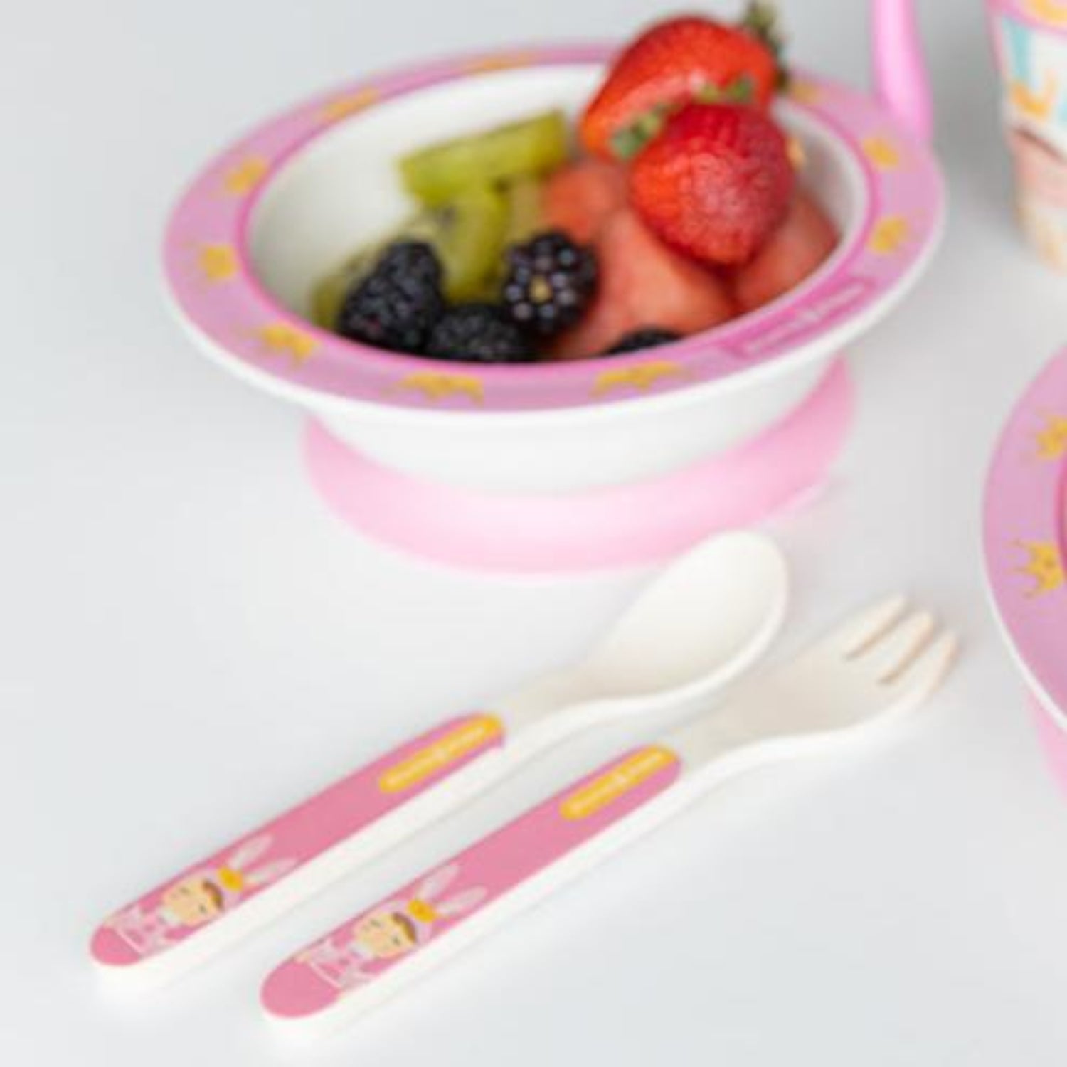 Close-up of a pink baby suction bowl filled with fresh fruit, paired with a matching spoon and fork. The BPA-free feeding set is designed for babies and toddlers learning to self-feed while making mealtime easier and less messy.