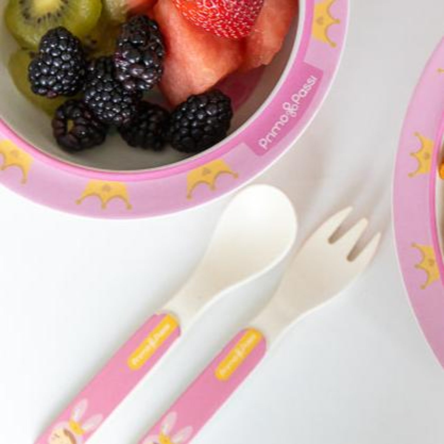 Children's bowl with fruit and pink utensils on a white background