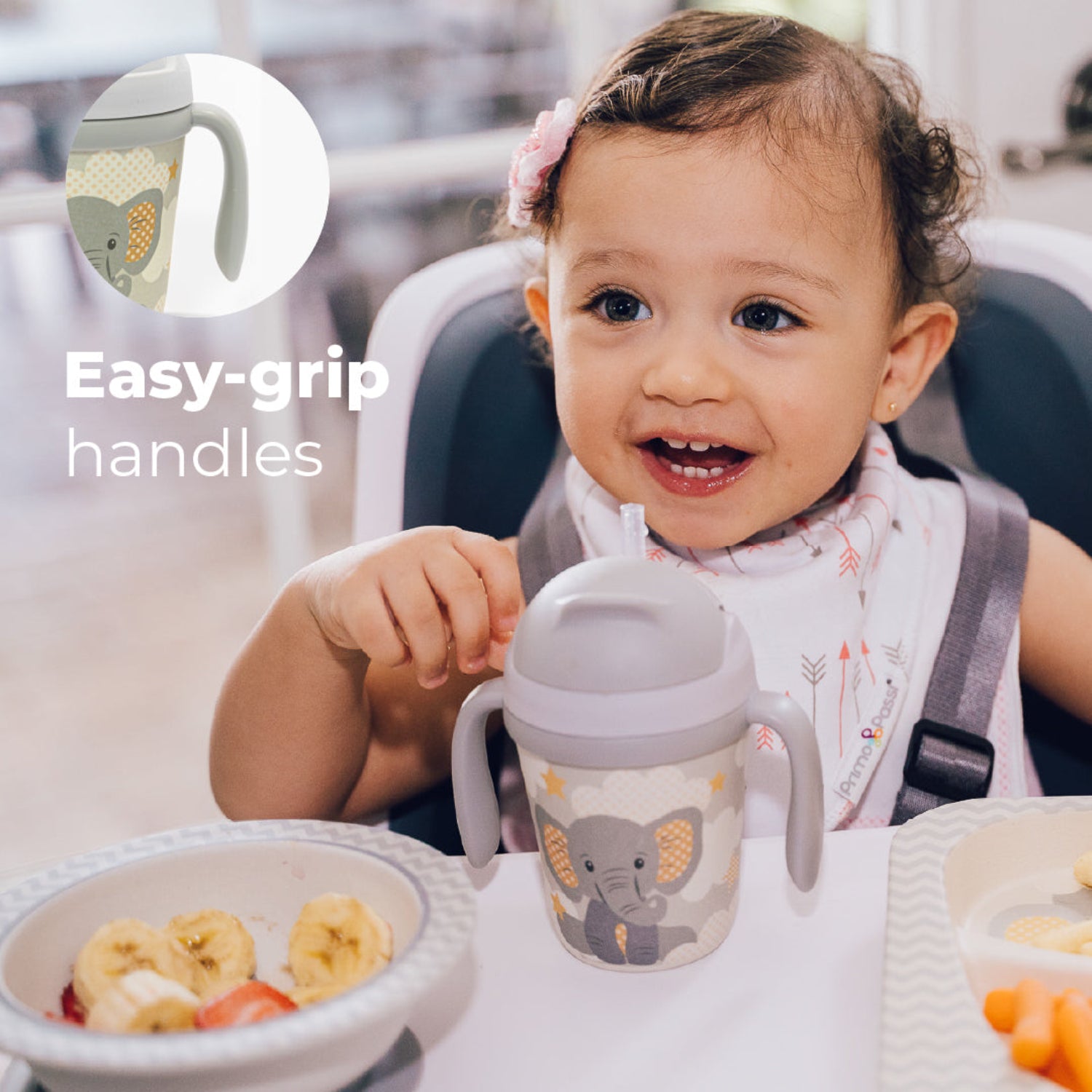 A little girl in a highchair with a Gray toddler training cup with two easy-grip handles, a soft straw, and a cute elephant illustration surrounded by clouds and stars on a light background with a text: easy-grip handles