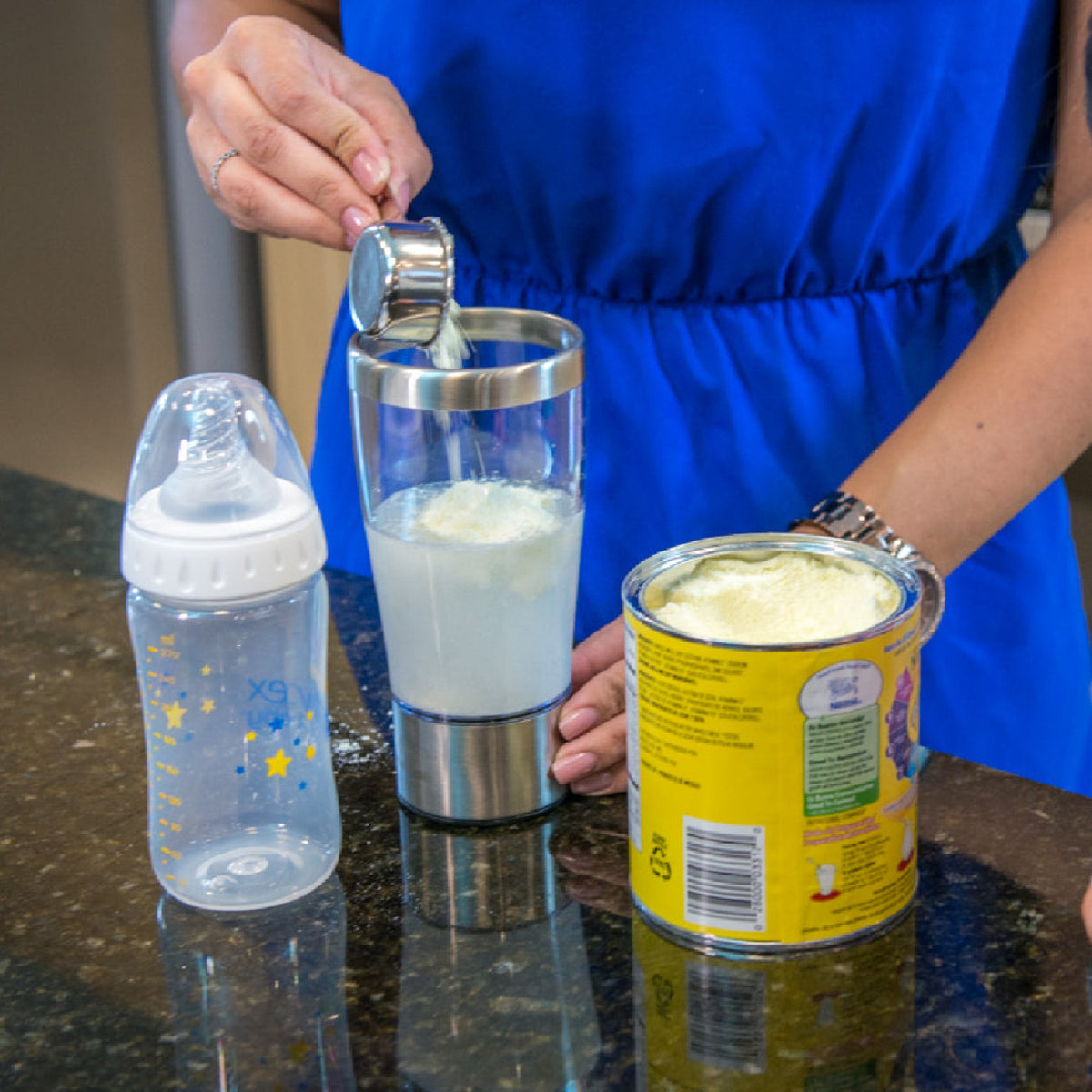 Parent adding baby formula powder to the Primo Passi portable electric formula mixer before blending. The rechargeable mixer is designed to quickly combine formula and water into a smooth, lump-free bottle with reduced air bubbles, making feeding preparation faster and more convenient at home or while traveling.
