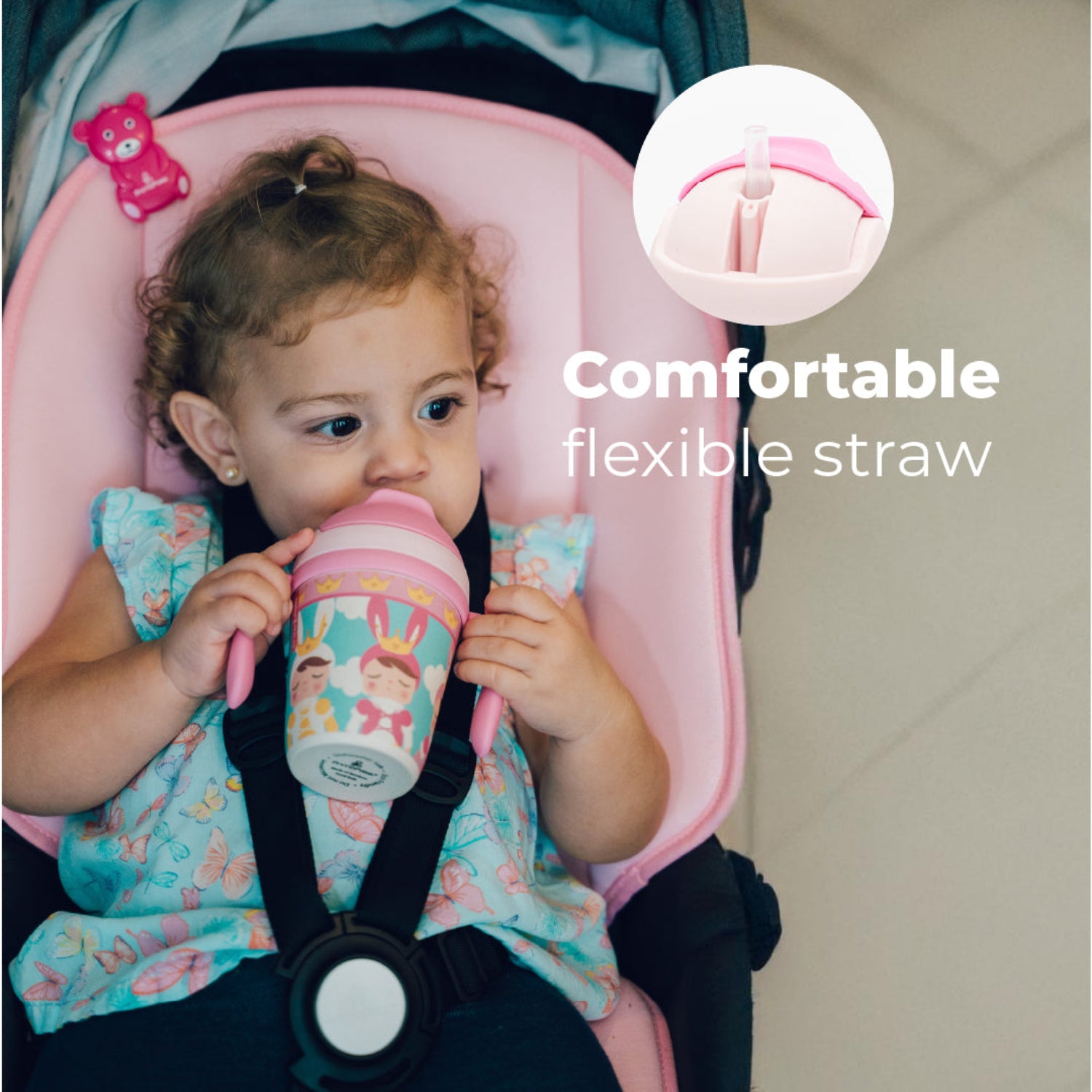 a little girl holding a Pink toddler training cup with two easy-grip handles, a soft straw, and a colorful princess-themed design featuring crowned characters, clouds, and crowns. With the text: Comfortable flexible straw