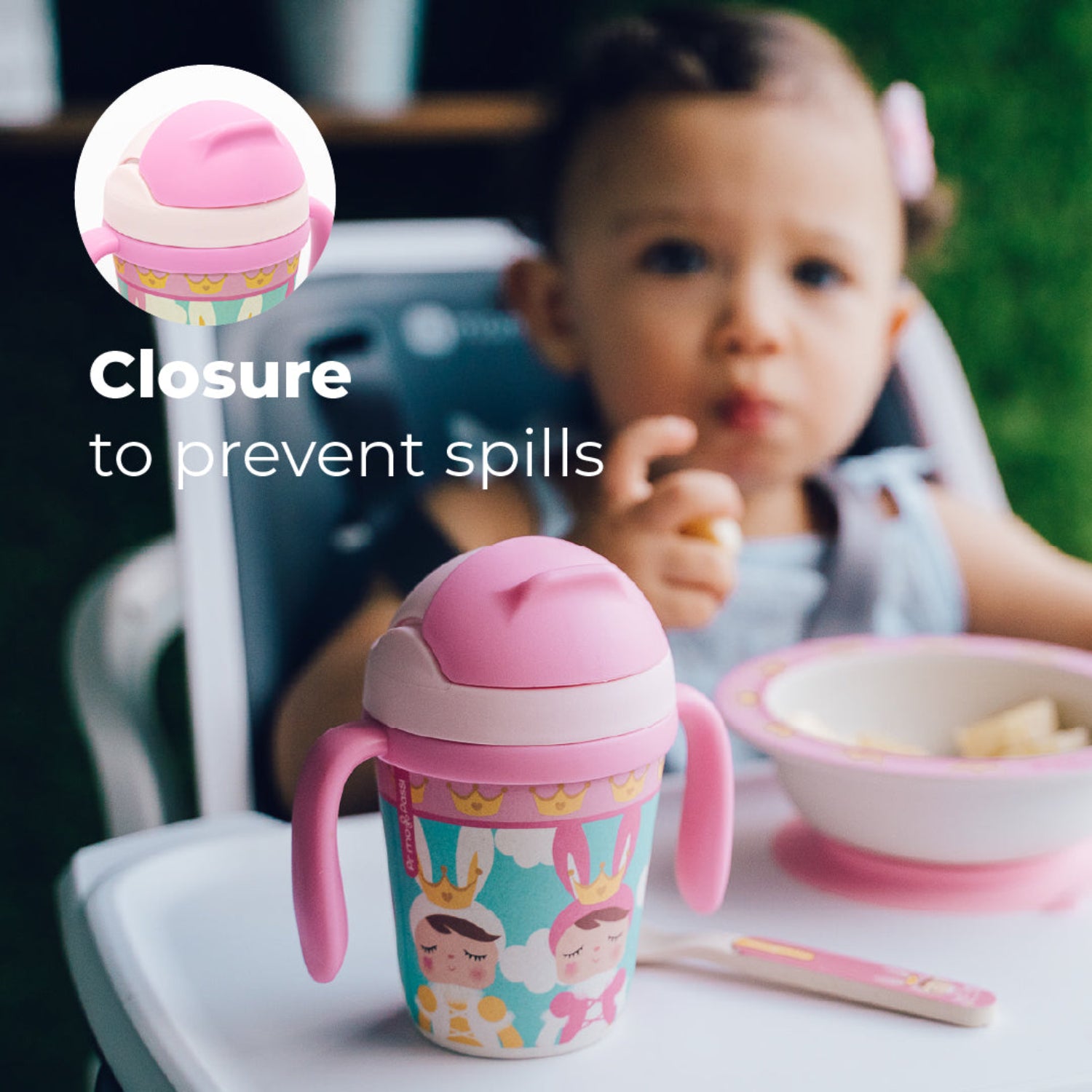 A young girl in a highchair with a Pink toddler training cup with two easy-grip handles, a soft straw, and a colorful princess-themed design featuring crowned characters, clouds, and crowns. with the text: Closure to prevent spills