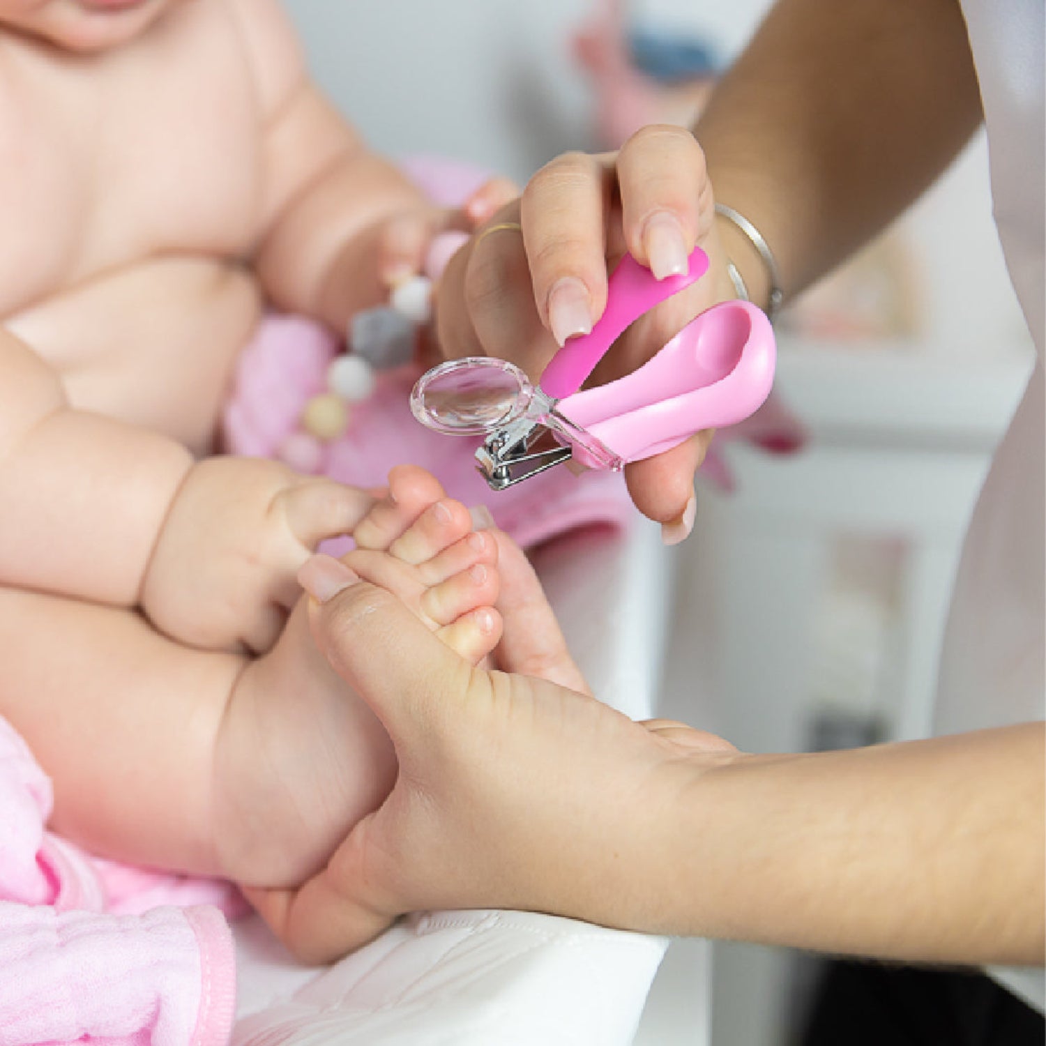 Person cutting a baby's toe nail with pink nail clippers.