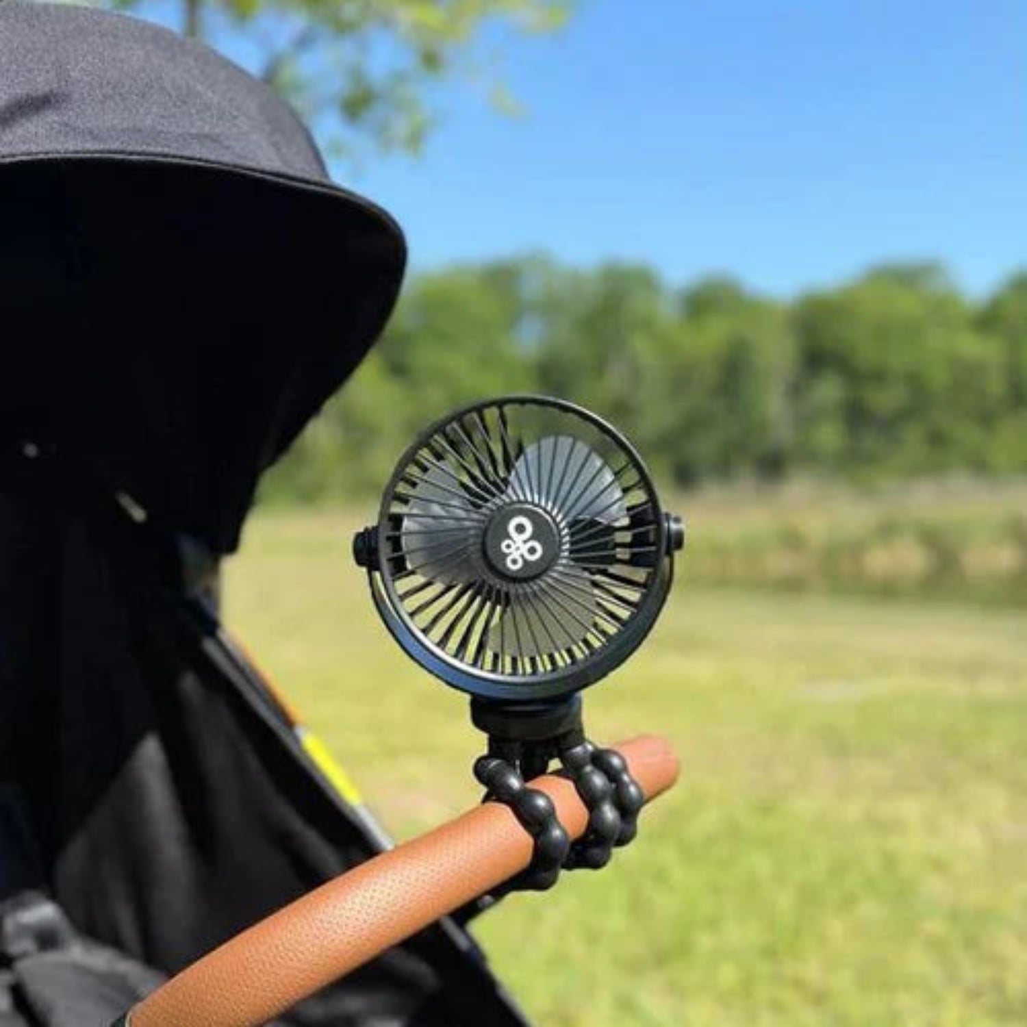 Portable fan attached to a stroller handle with a blurred outdoor background
