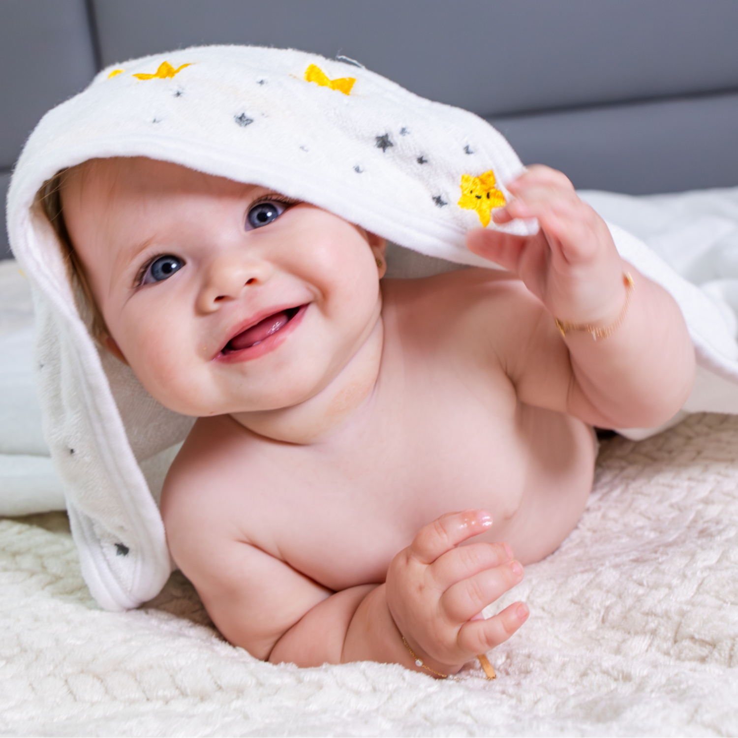 Baby wearing a white hood with yellow stars, lying on a soft surface.