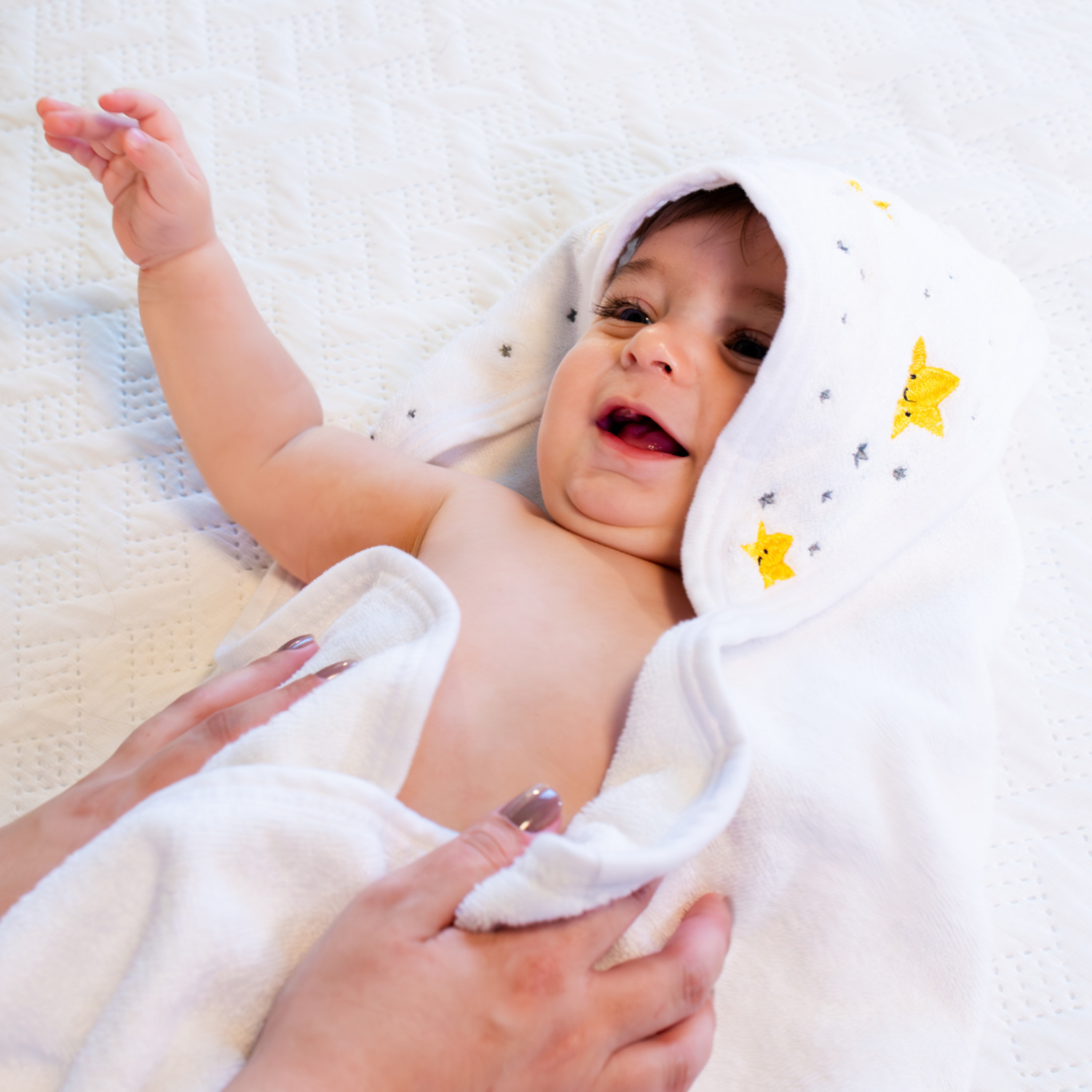 Baby wrapped in a white towel with star patterns, lying on a soft surface.