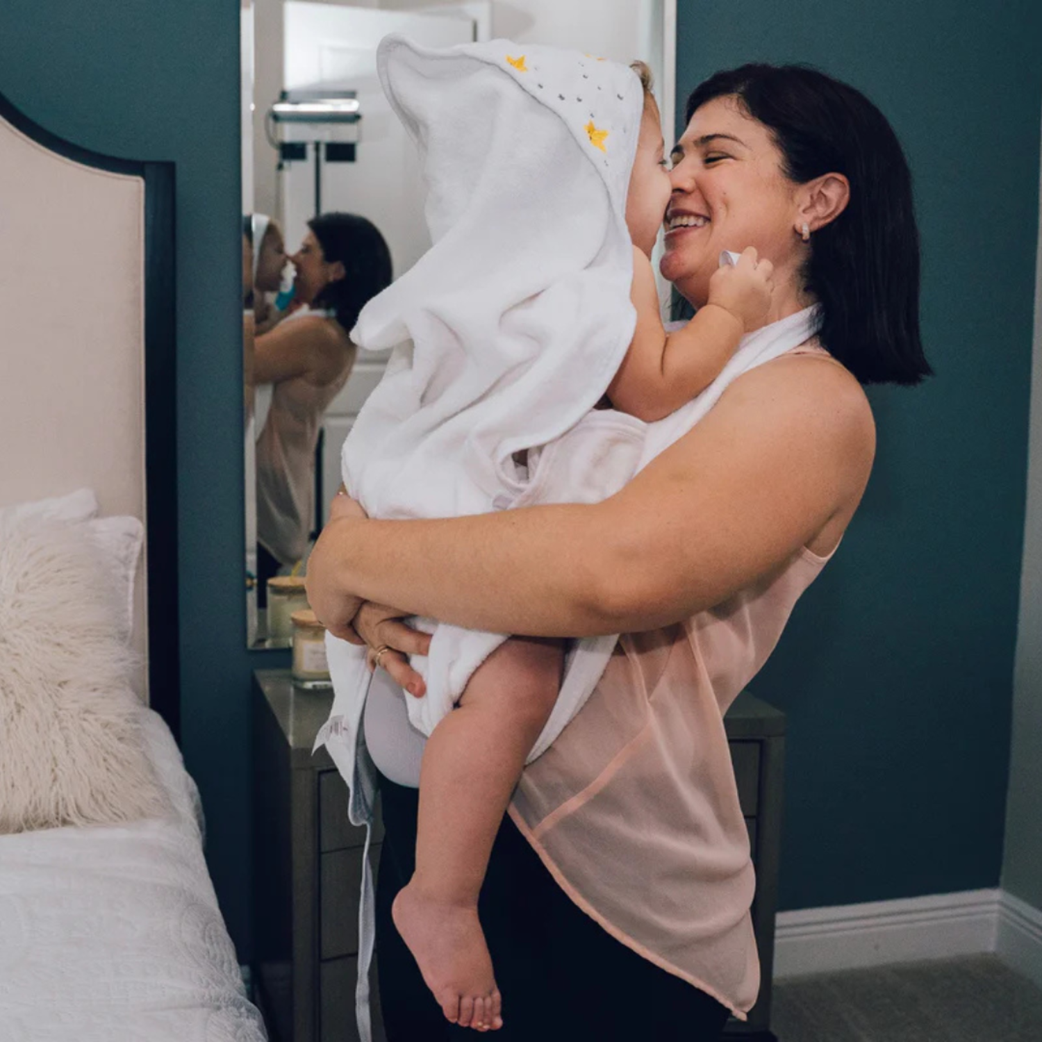 Woman holding a baby wrapped in a towel in a bedroom setting