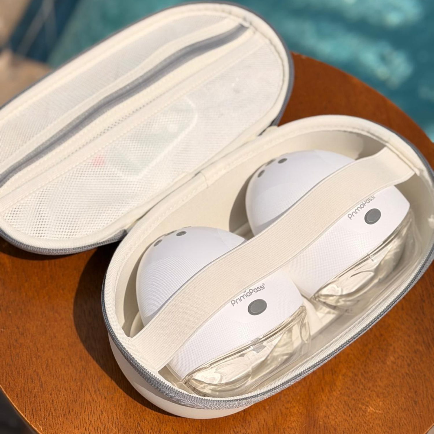 Electric Hands-Free Breast Pump in an open beige case on a wooden surface with a blurred pool background.