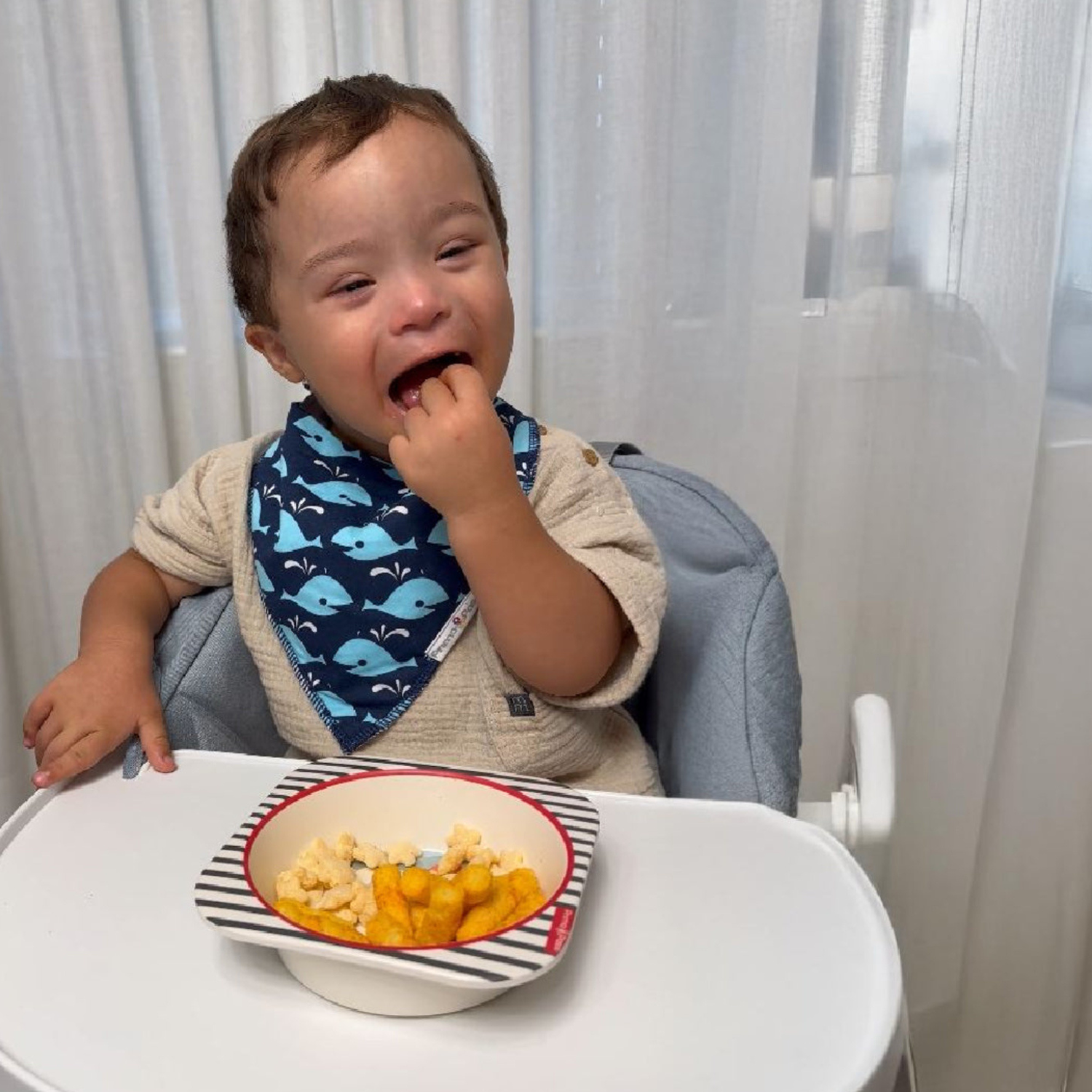 A smiling toddler sits in a high chair enjoying a snack served in a bamboo fiber children's bowl with a playful arctic-themed design. The lightweight, eco-friendly bowl is ideal for everyday meals and snacks, making mealtime fun for little ones.