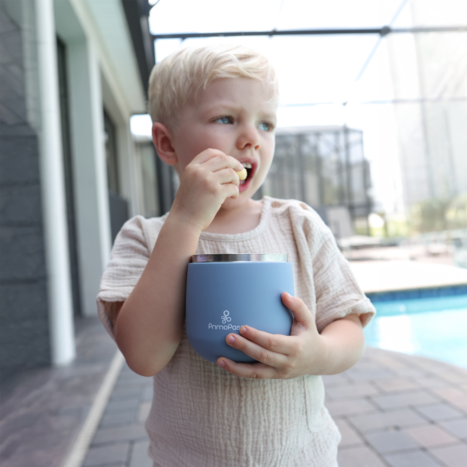 Child holding a blue food jar outdoors near a pool