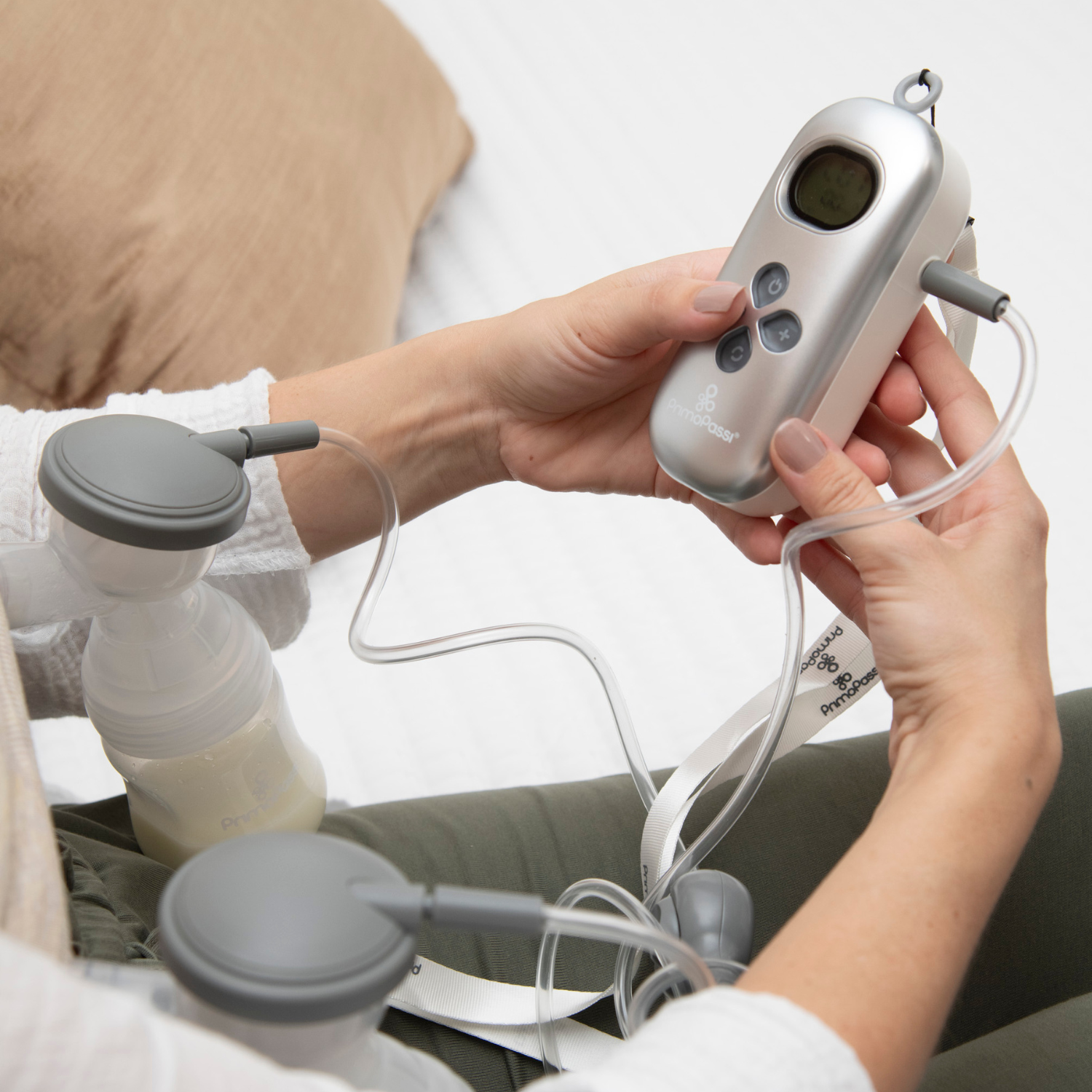 Close-up of a mom using the Primo Passi Portable Dual Charge Electric Breast Pump, adjusting the rechargeable control unit while double pumping. The portable breast pump features customizable suction settings for comfortable, efficient milk expression at home or on the go.