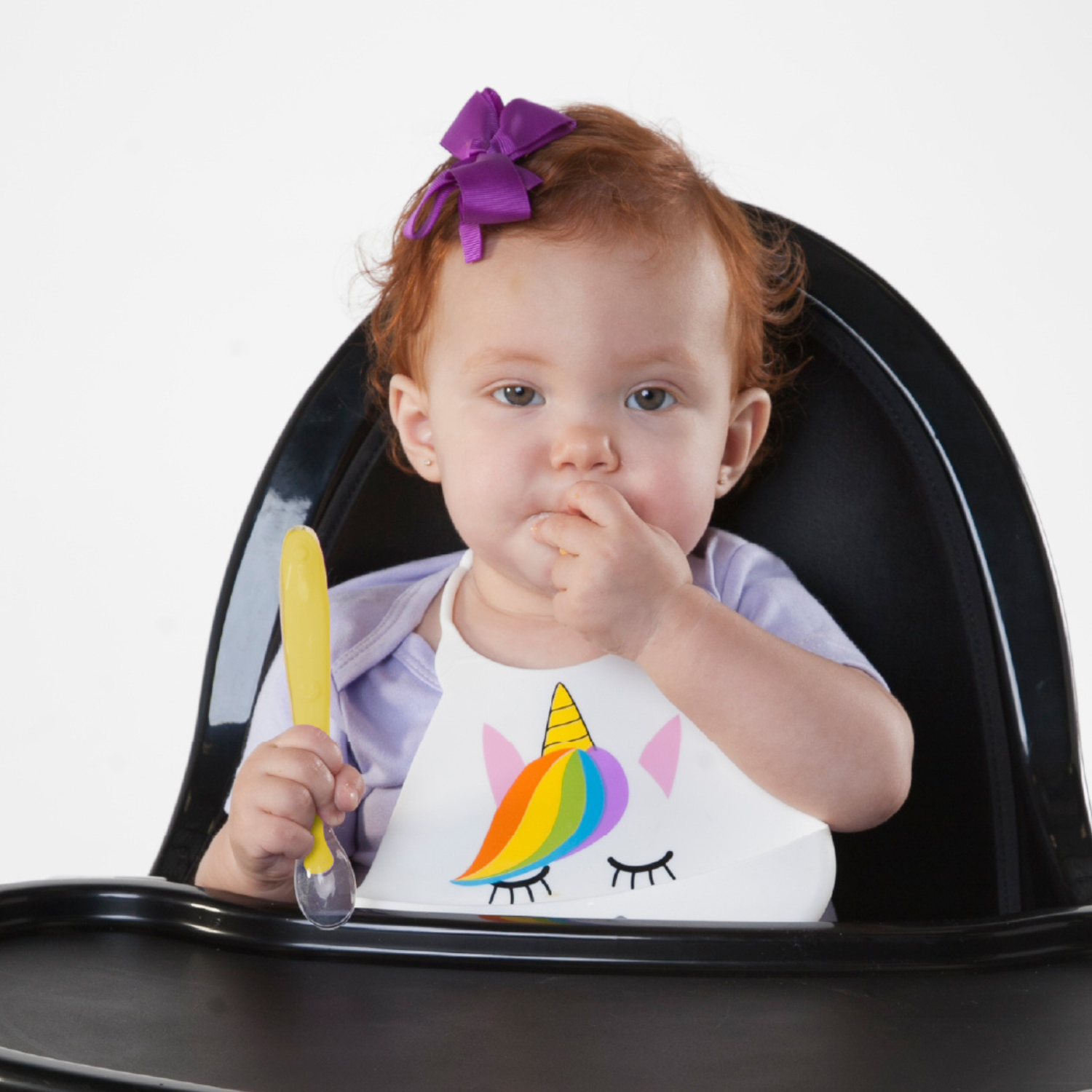 Four Primo Passi silicone baby spoons in pink and yellow with transparent spoon tips on a white background, highlighting the long handles for an easy grip for baby's hands.