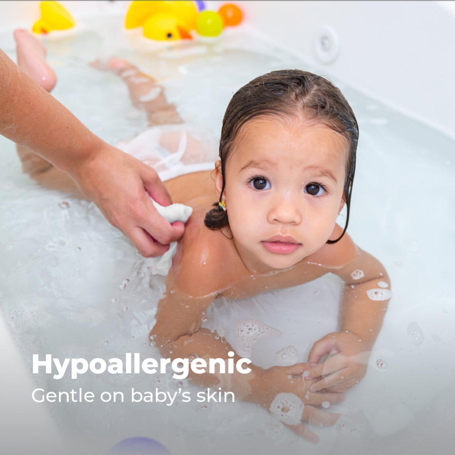 A young child enjoys bath time while an adult gently cleans their back with a soft white muslin washcloth. The image highlights the hypoallergenic washcloth, designed to be gentle on a baby's delicate skin.