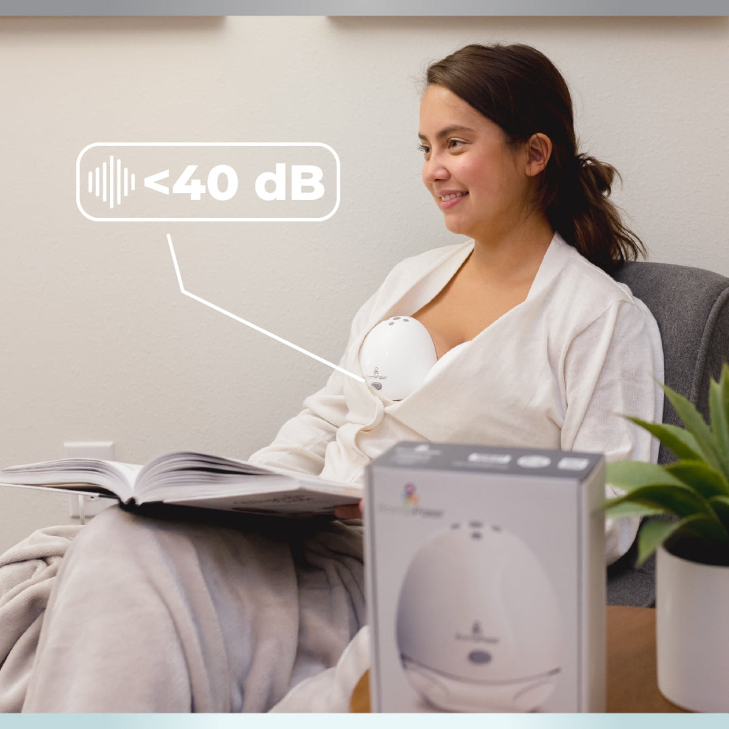 Woman reading a book with an Electric Hands-Free Breast Pump on her and the box next to her, indicating a quiet environment - less then 40dB