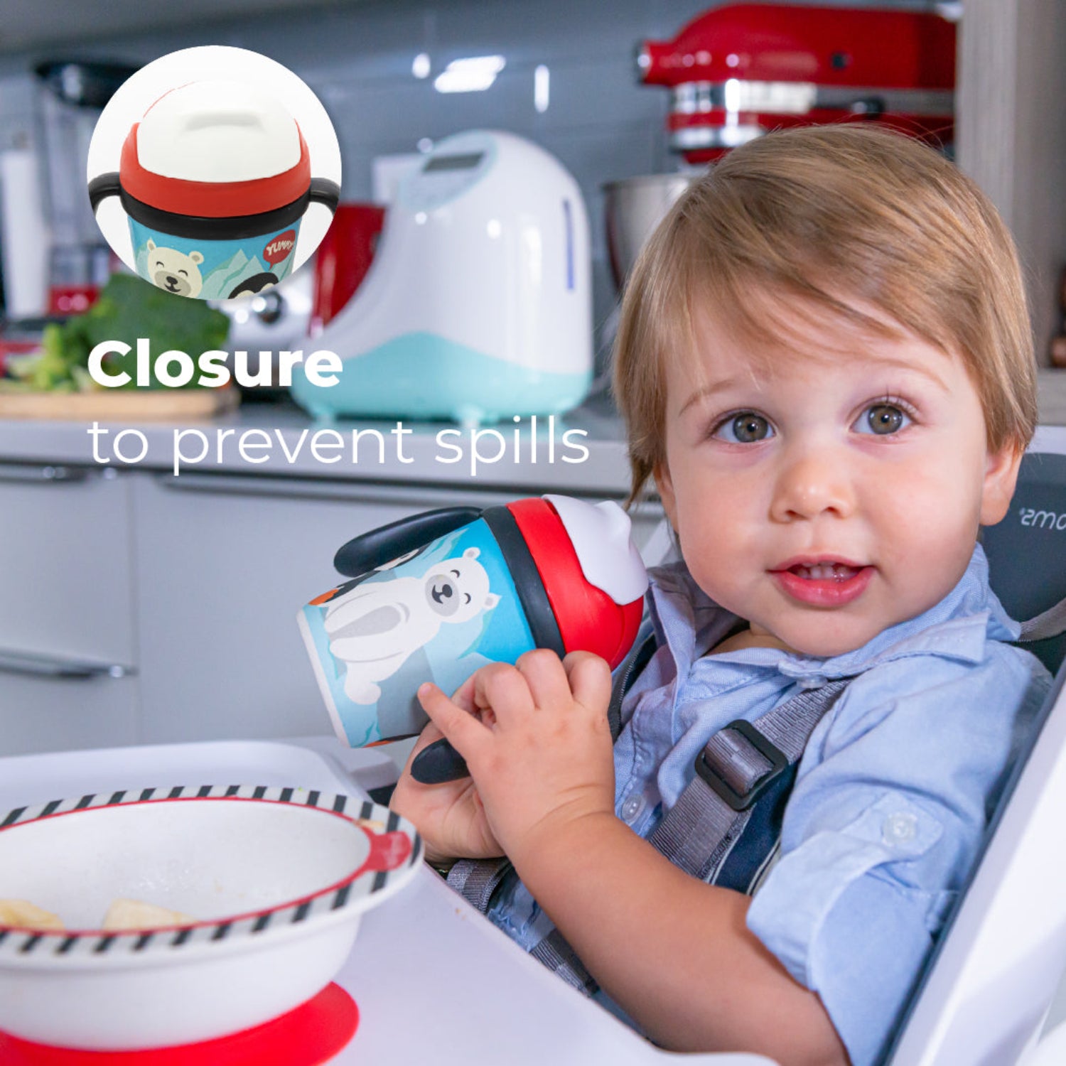 A little boy in a highchair holding a Red toddler training cup with two easy-grip handles, a soft straw, and a playful arctic-themed design featuring a smiling polar bear and penguin against snowy mountains in a kitchen background with the text: Closure to prevent spills