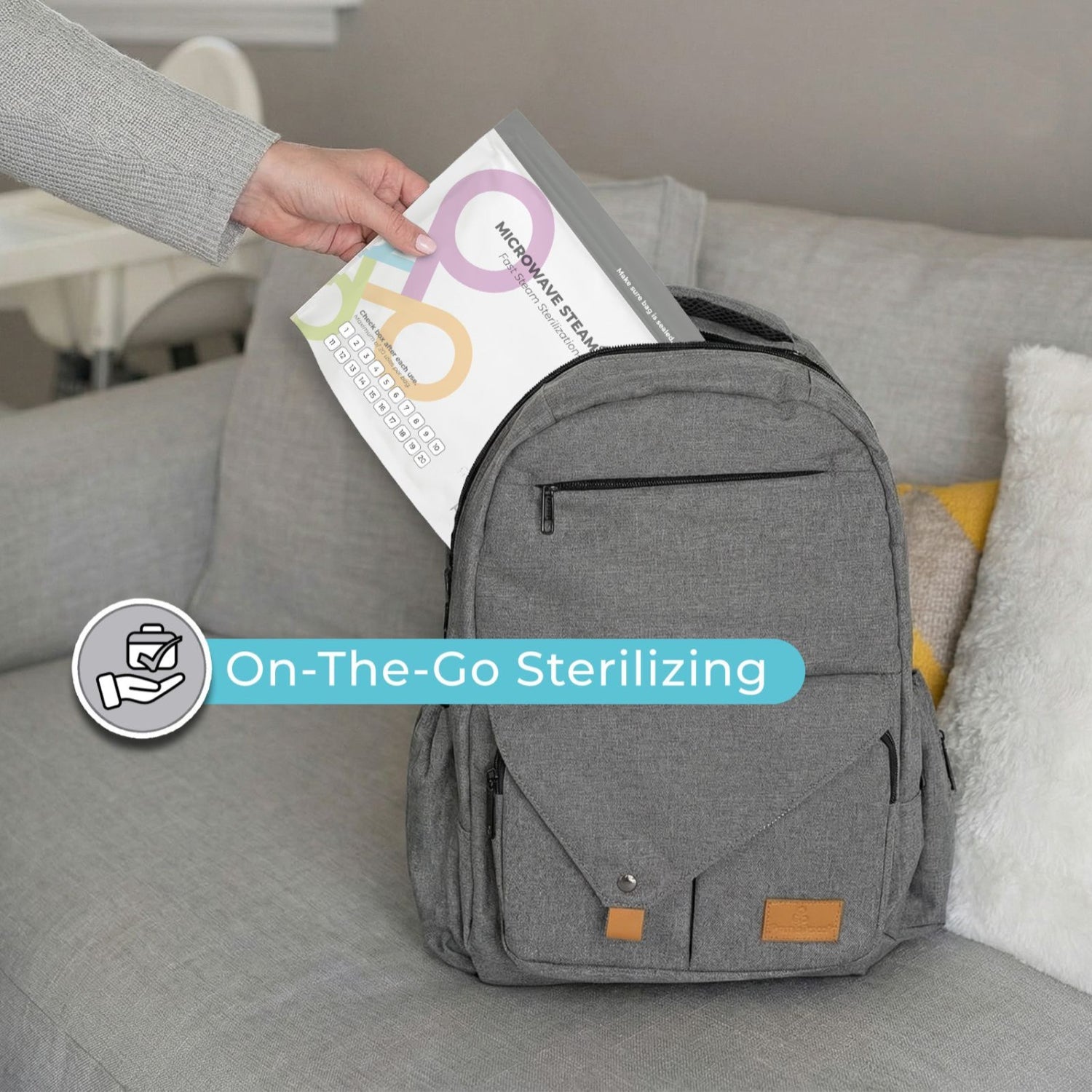 Gray backpack on a couch with a hand placing microwave steam sterilizer bags into it, labeled 'On-The-Go Sterilizing'.