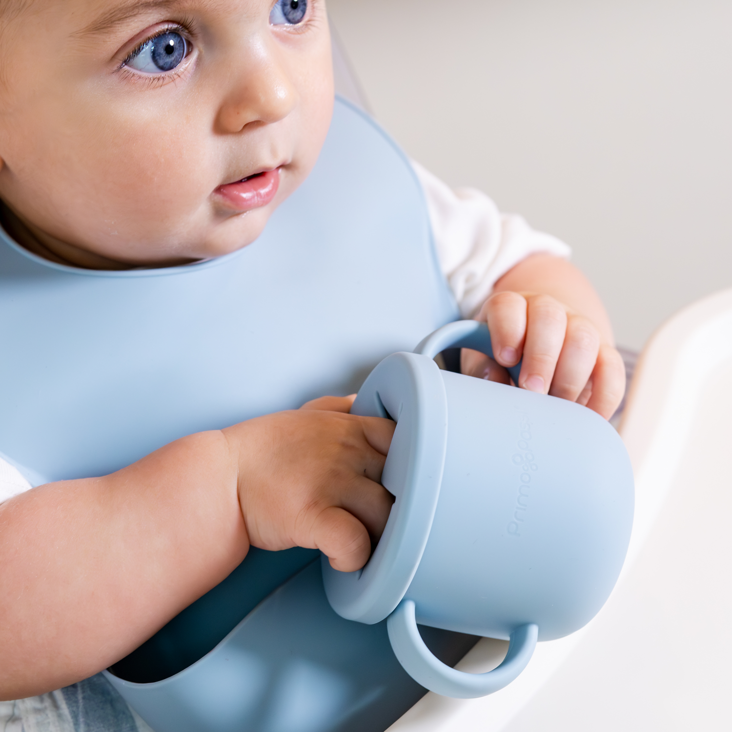 Baby wearing a blue bib holding a blue cup