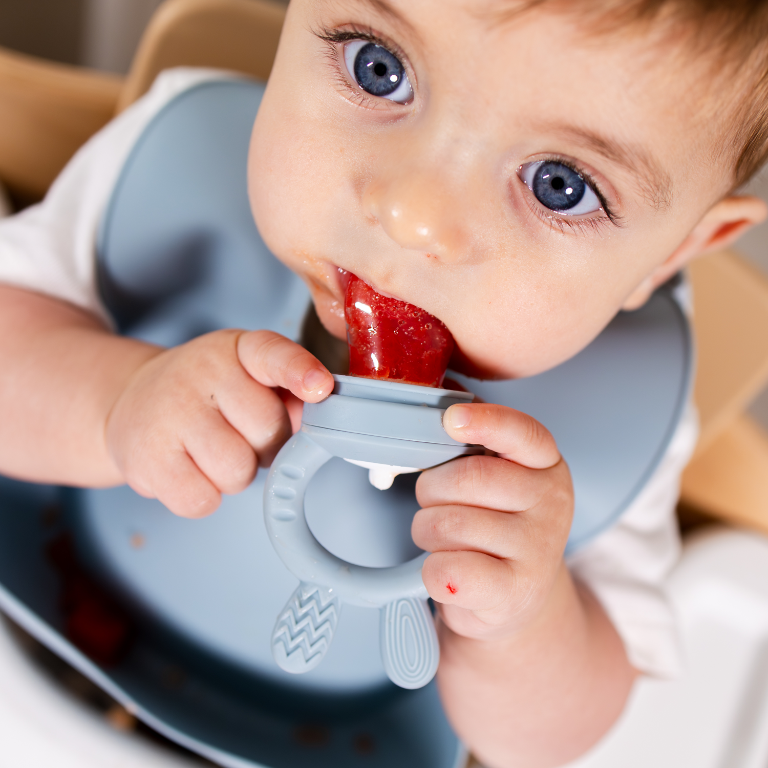 Baby using a food feeder with strawberry in it and with a blue bib