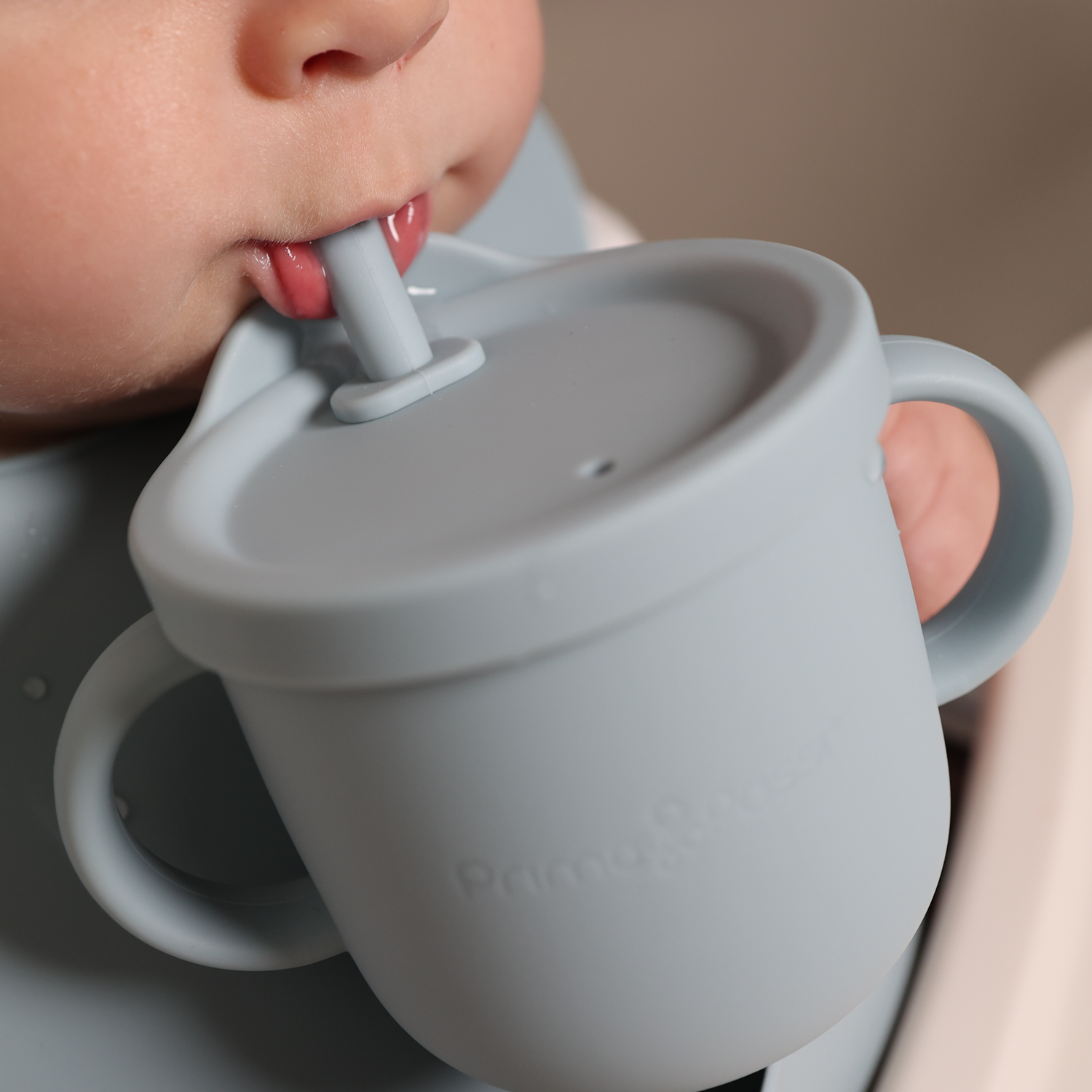 Baby holding and drinking on a blue silicone training cup with a straw