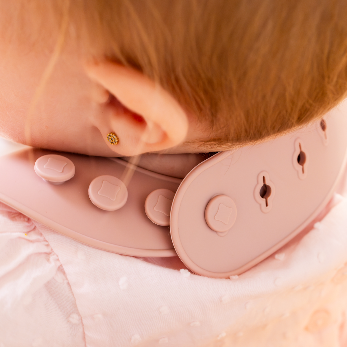 Close-up of a baby wearing a pink silicone bib with buttons.