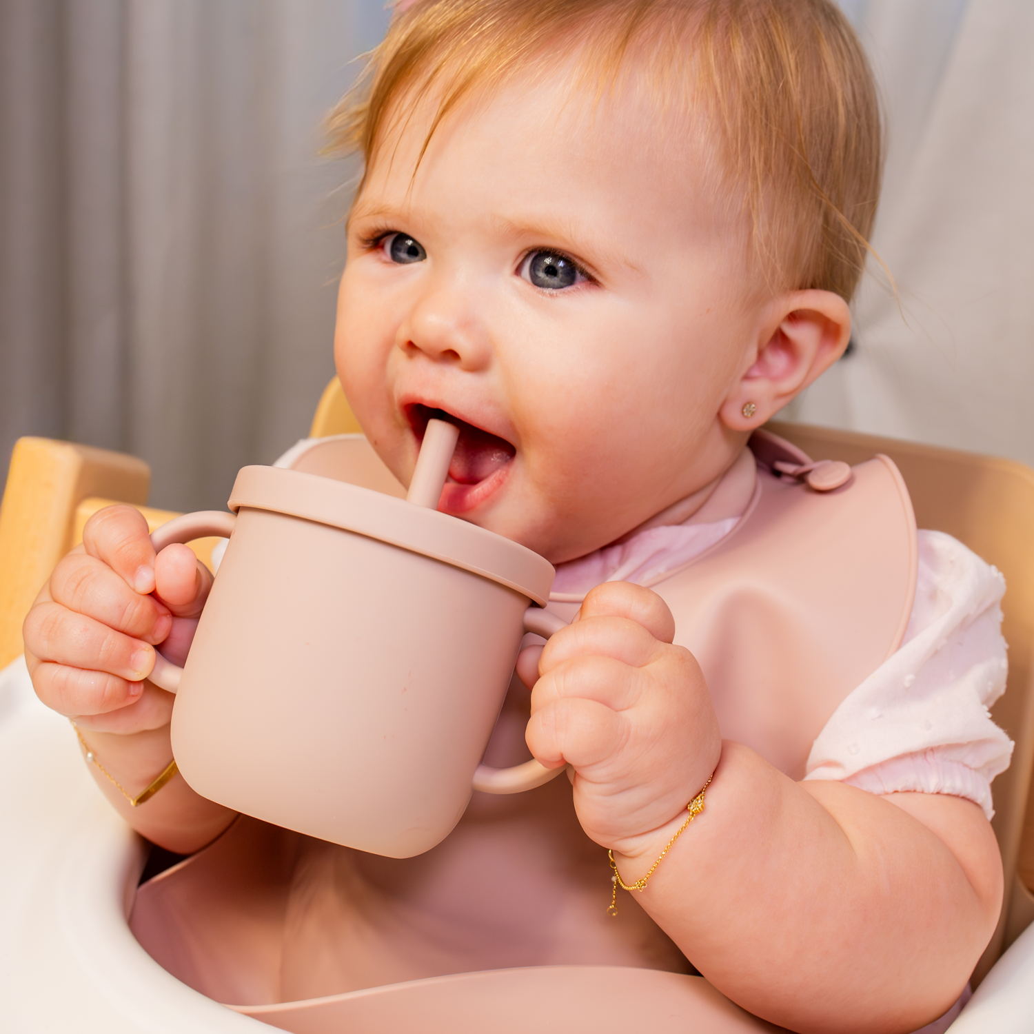 Baby holding a pink silicone training cup with a straw