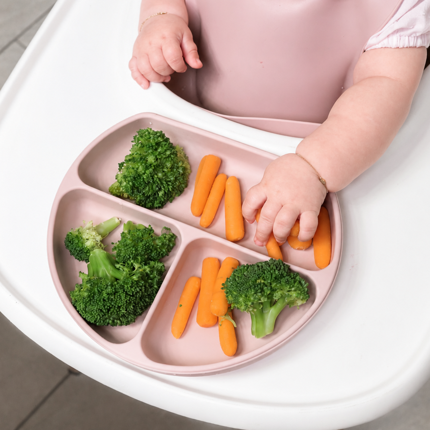 Child reaching for carrots on a divided pink silicone plate with broccoli