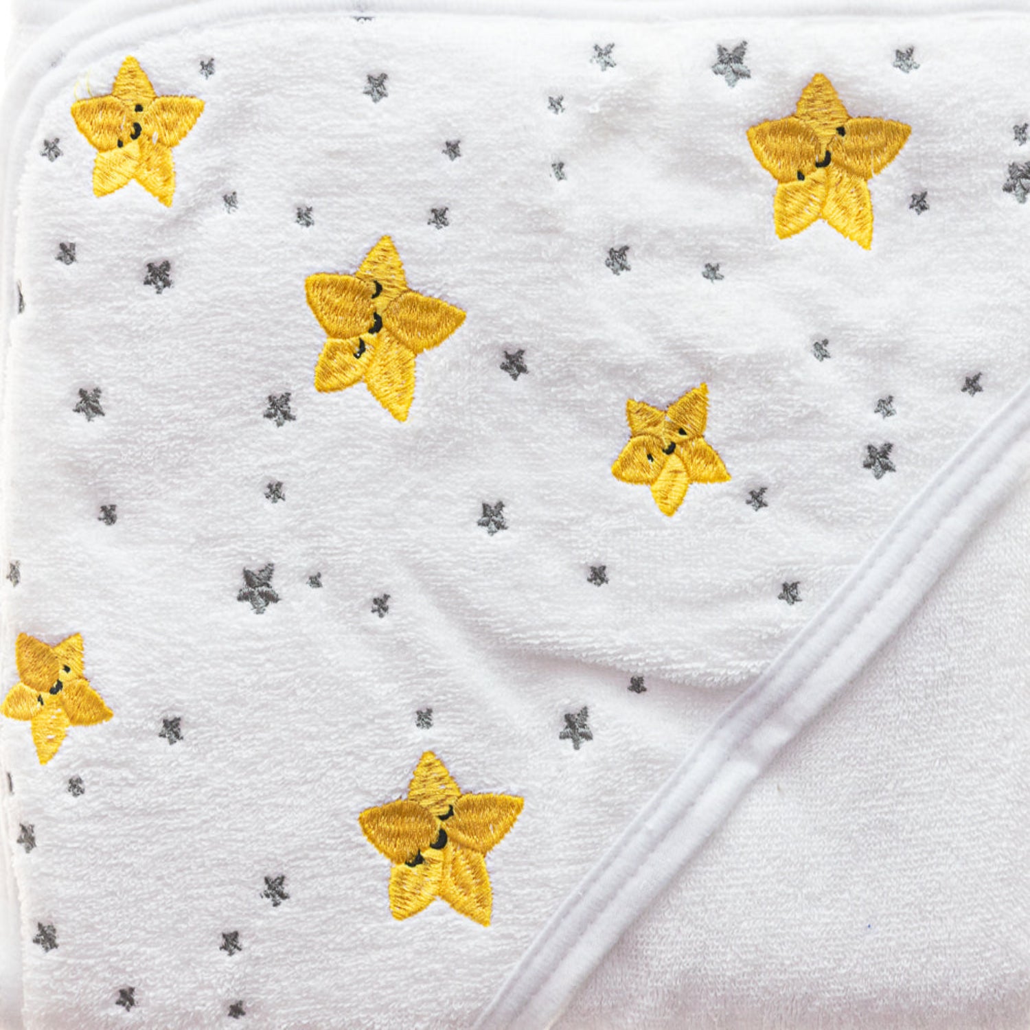 Close-up of a white hooded baby towel featuring embroidered yellow stars and a soft plush texture. Made with absorbent, gentle fabric, this cozy towel helps keep babies warm and dry after bath time.