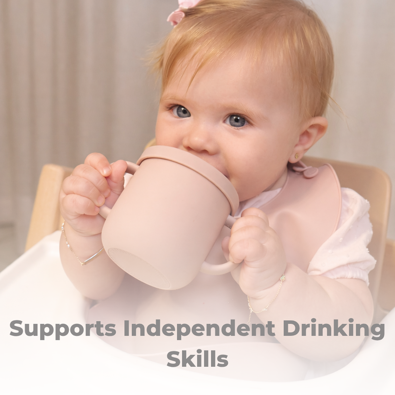 Baby holding a pink cup with text 'Supports Independent Drinking Skills' on a neutral background