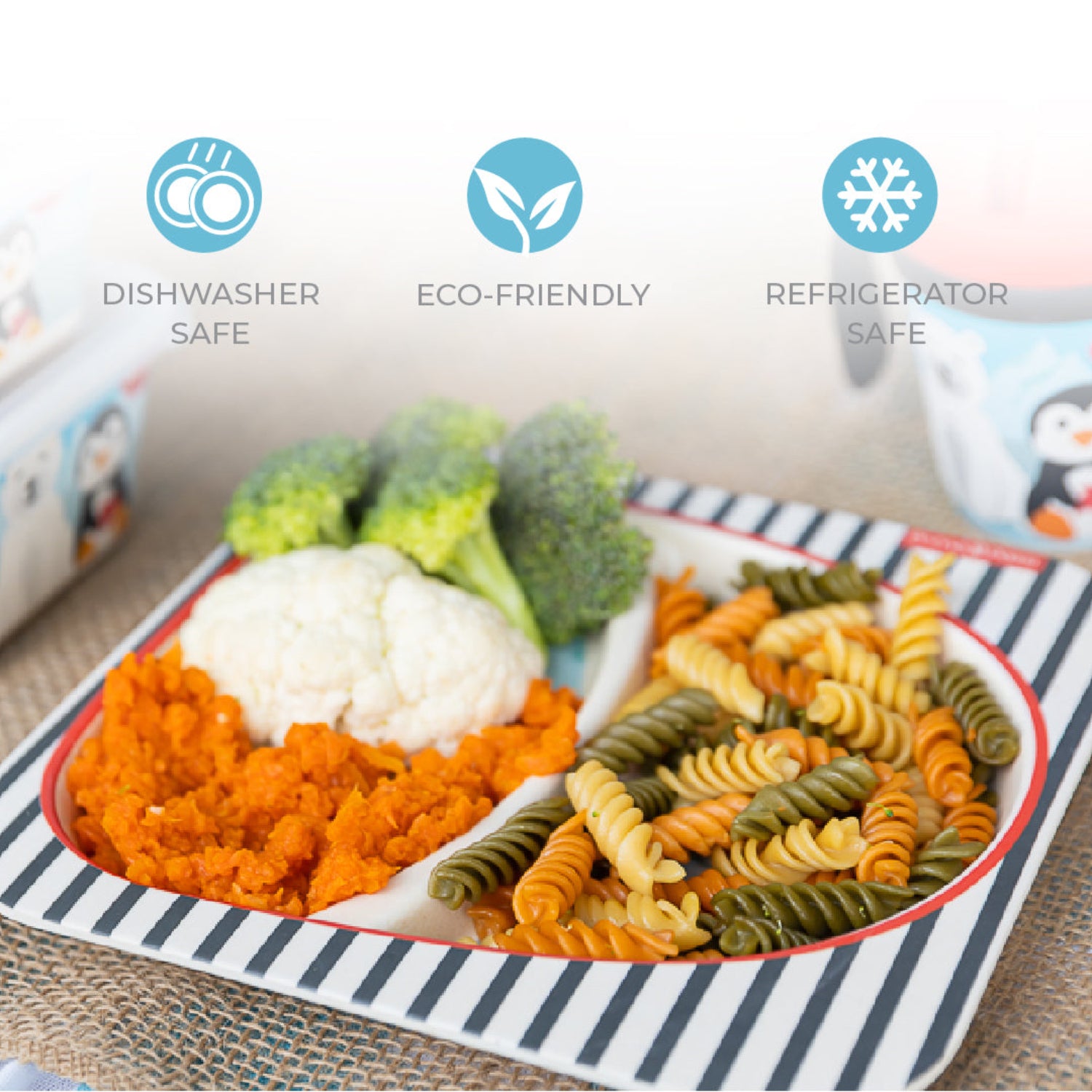 A divided plate with a polar bear and penguin print with food in it, shown on a woven mat with promotional text icons for dishwasher safe, eco-friendly, and refrigerator safe.