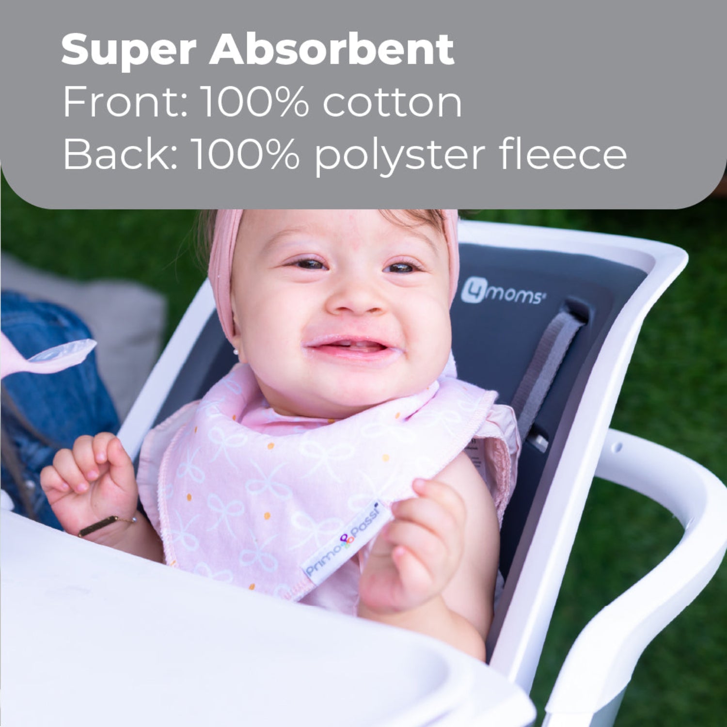 Smiling baby wearing a Primo Passi pink bandana bib with a delicate bow pattern while sitting in a high chair. The bib features a highly absorbent 100% cotton front and a soft 100% polyester fleece backing to help keep babies dry and comfortable during feeding, drooling, and teething. Suitable for babies 0–9 months.
