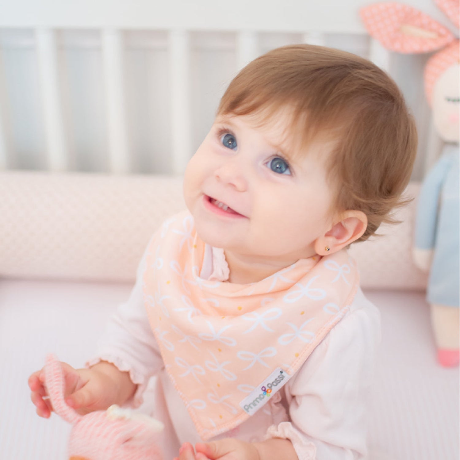 Baby wearing a pink bib with a brand logo, sitting on a white surface.
