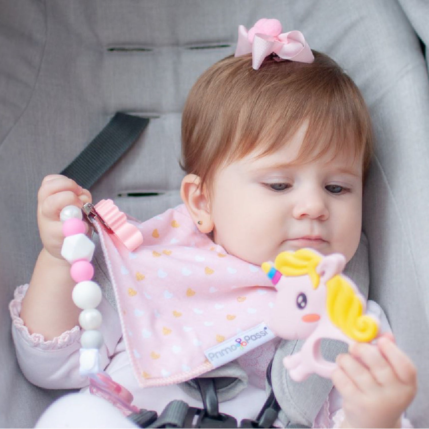 Baby in a car seat wearing a pink bib and holding a teething toy.
