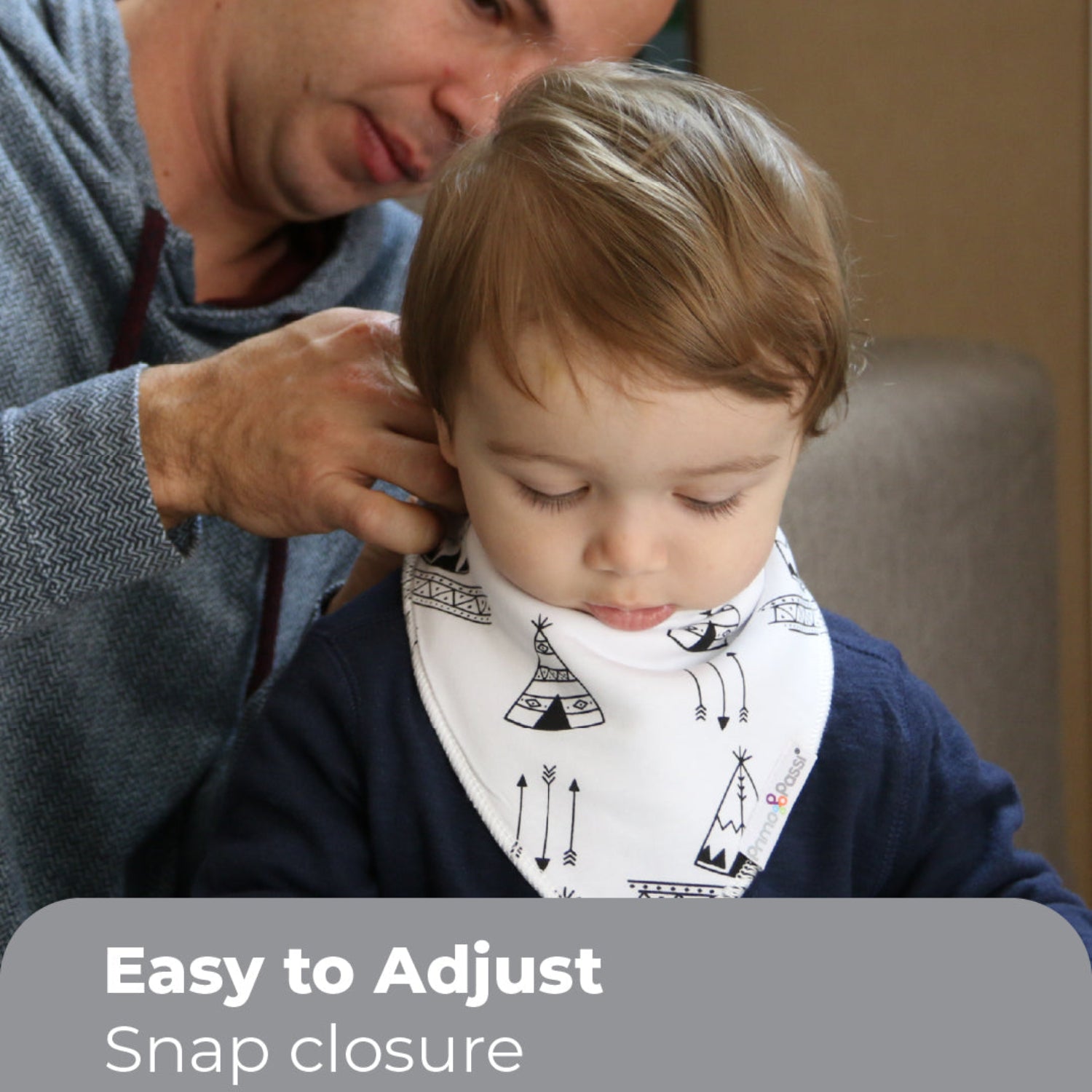 A parent adjusts a Primo Passi bandana bib with a black-and-white teepee and arrow print on a toddler. The bib features an easy snap closure for a secure, adjustable fit, keeping little ones comfortable during meals and drooling.