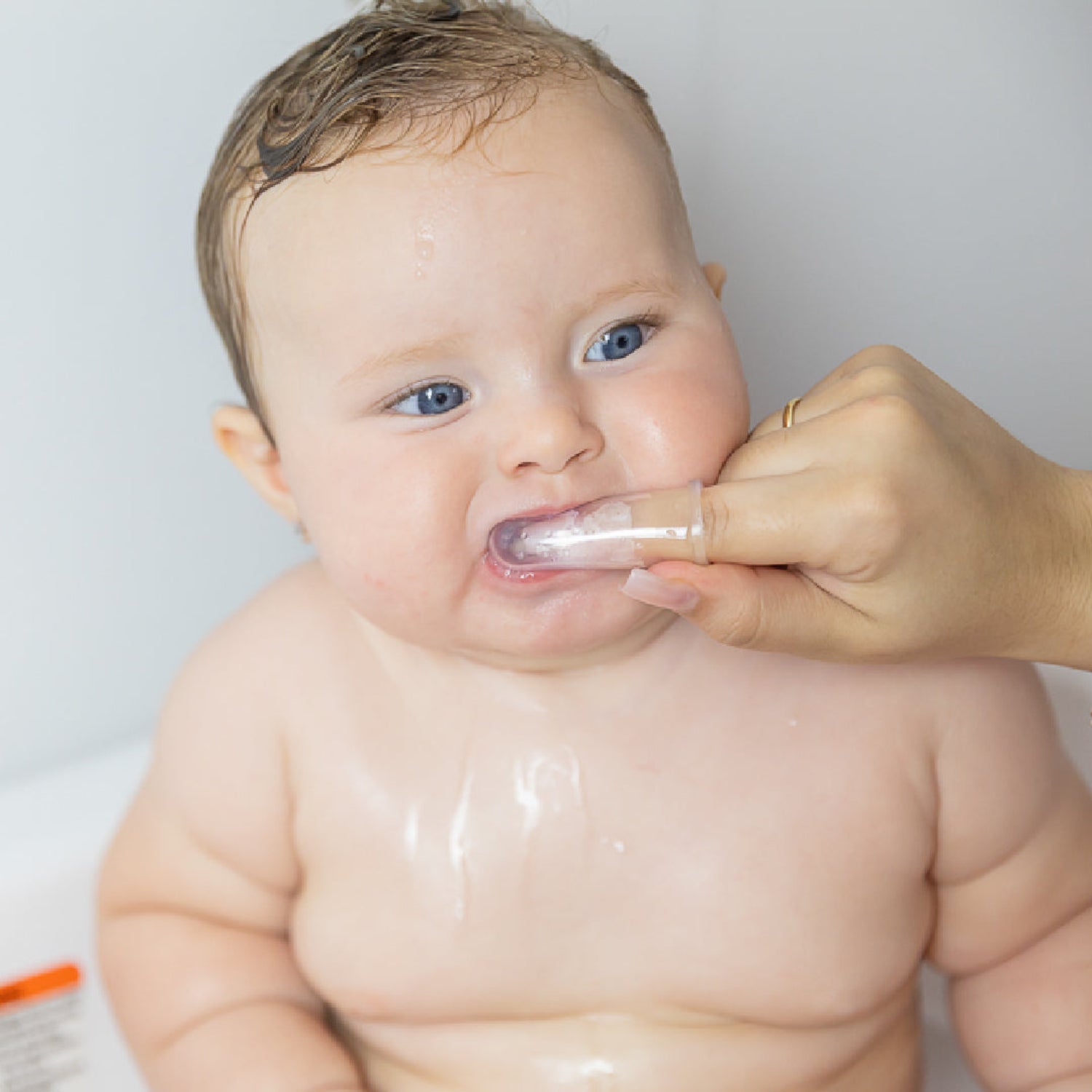 Parent using the Primo Passi silicone finger toothbrush to gently clean a baby's teeth and massage delicate gums during bath time. The soft, 100% food-grade silicone finger brush fits securely over an adult finger for safe, gentle oral care and early dental hygiene. Suitable for babies 3 months and older.