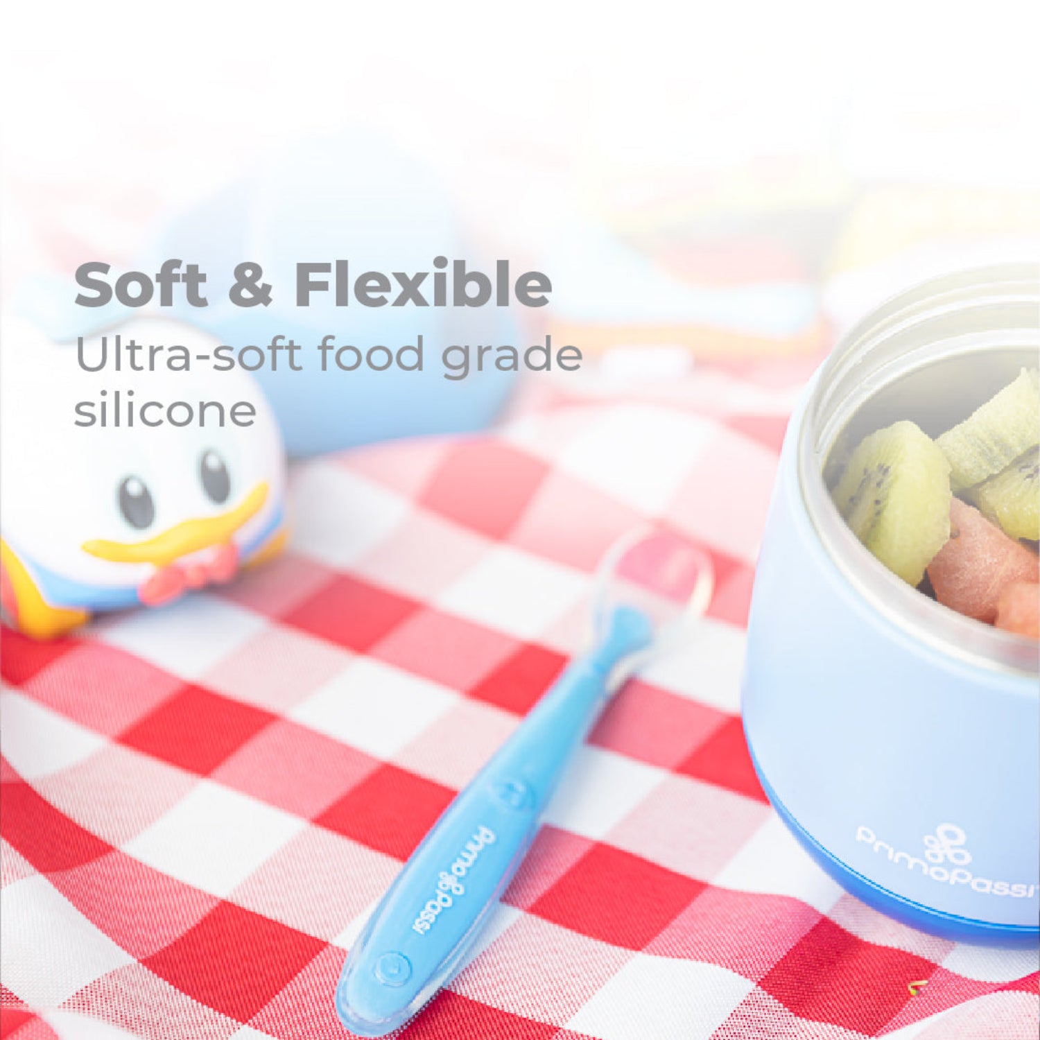 Baby blue silicone spoon and  blue bowl on a checkered tablecloth with text about soft flexible silicone material.