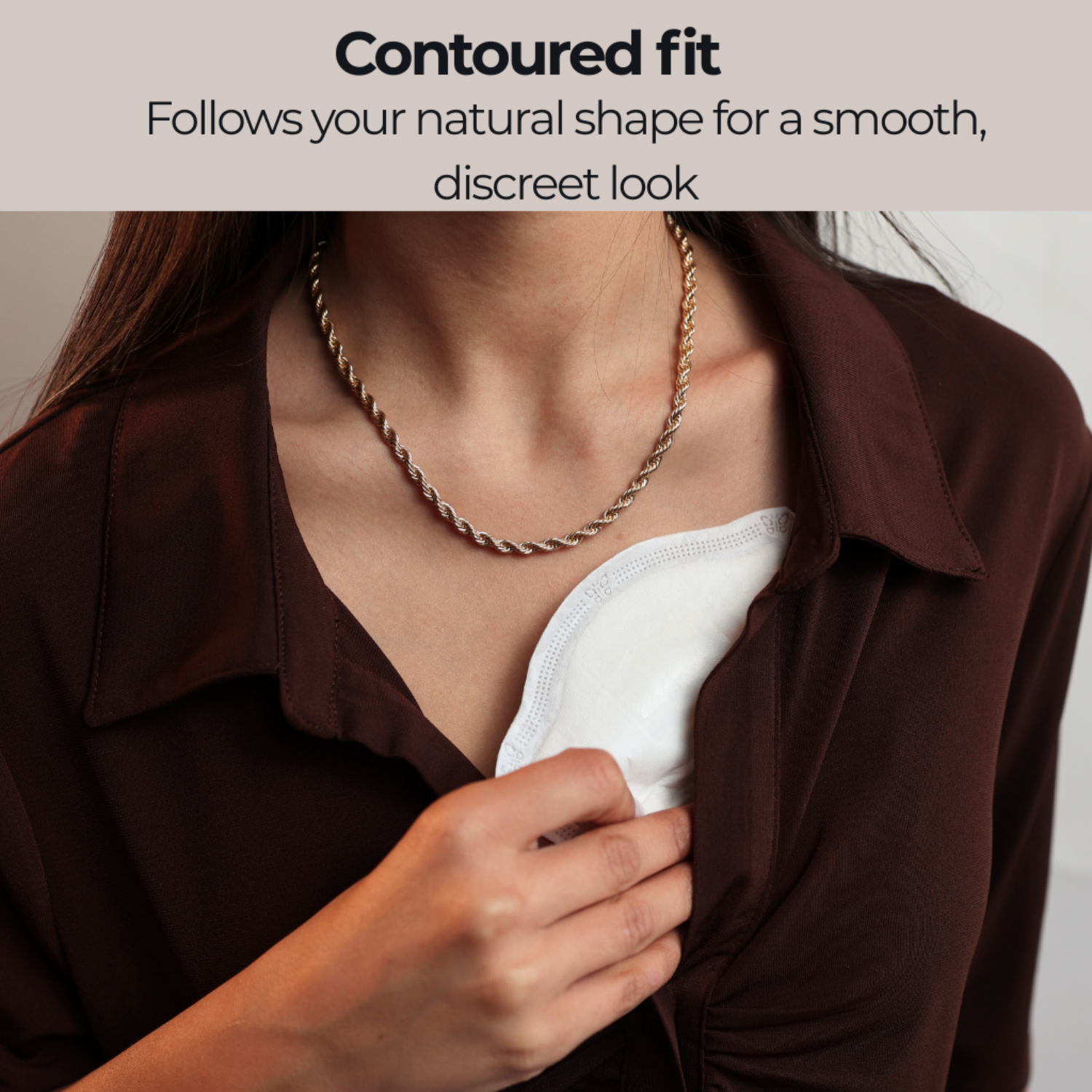 Close-up of a woman placing a Primo Passi disposable nursing pad inside her bra. The contoured nursing pad follows the natural shape of the breast for a smooth, discreet fit under clothing while providing reliable leak protection and all-day comfort for breastfeeding moms.