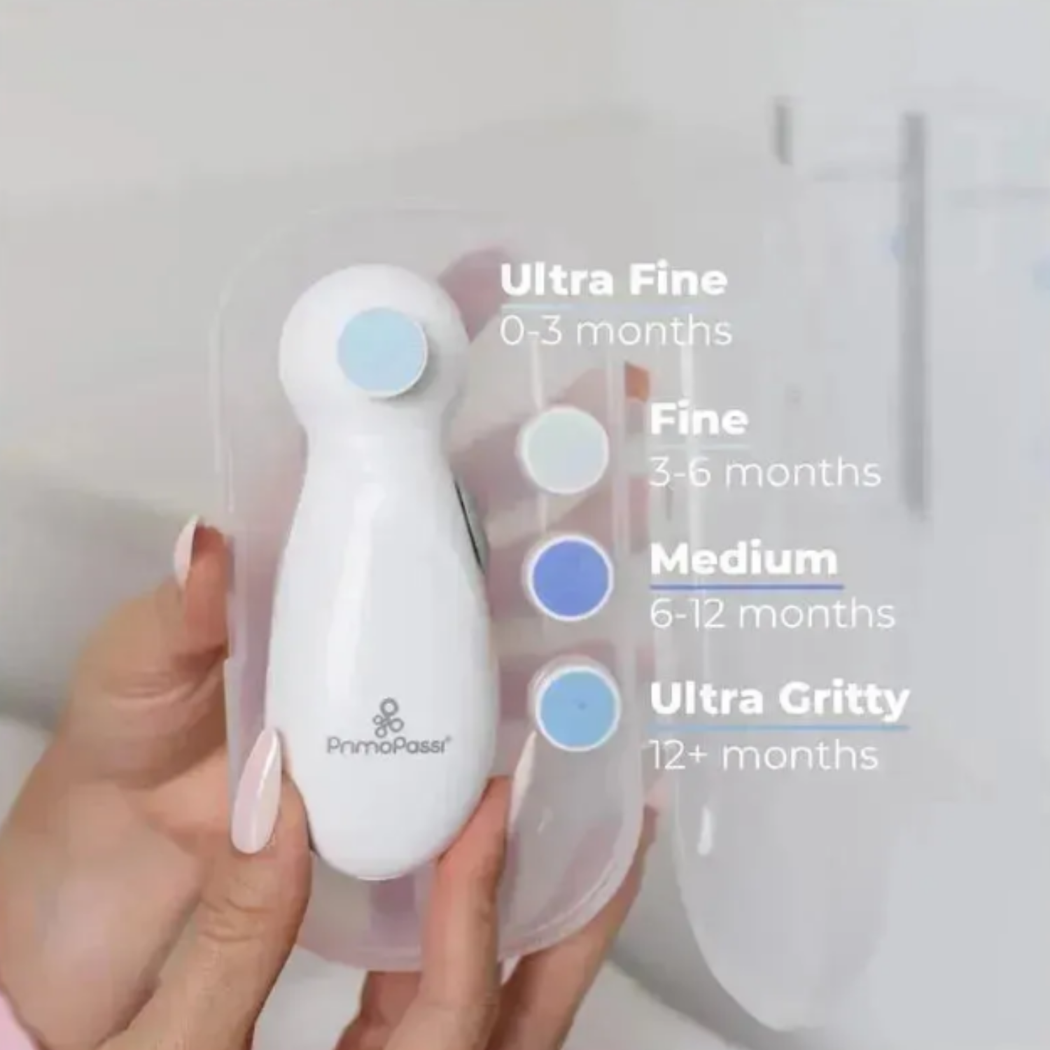 Close-up of the Primo Passi Baby Electric Nail Filer held in hand with four color-coded filing pads displayed beside it. On-screen text identifies the pads by age: Ultra Fine (0–3 months), Fine (3–6 months), Medium (6–12 months), and Ultra Gritty (12+ months).