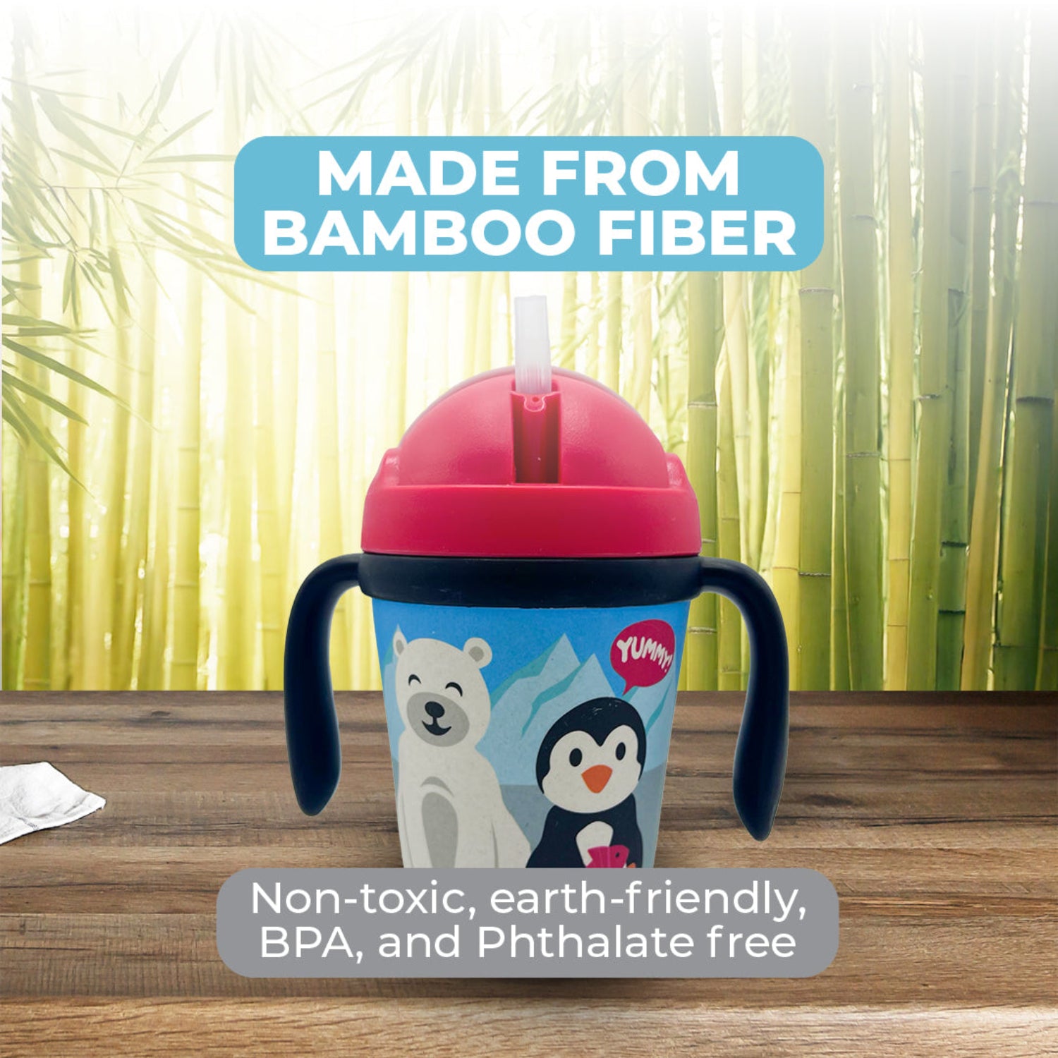 Red toddler training cup with two easy-grip handles, a soft straw, and a playful arctic-themed design featuring a smiling polar bear and penguin against snowy mountains. The spill-resistant cup is shown on a green and wood background.
