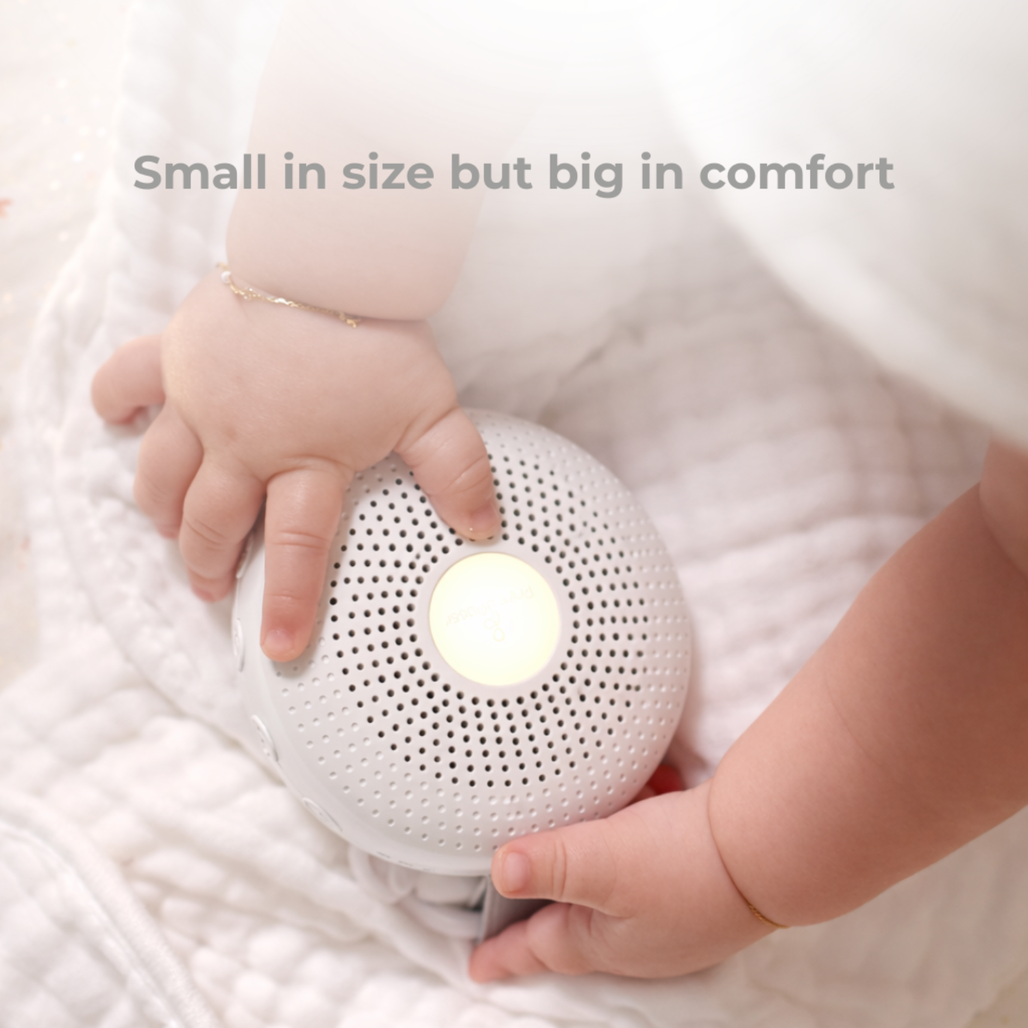 white portable sound machine for babies held by a child's hand on a white blanket with text 'Small in size but big in comfort'.