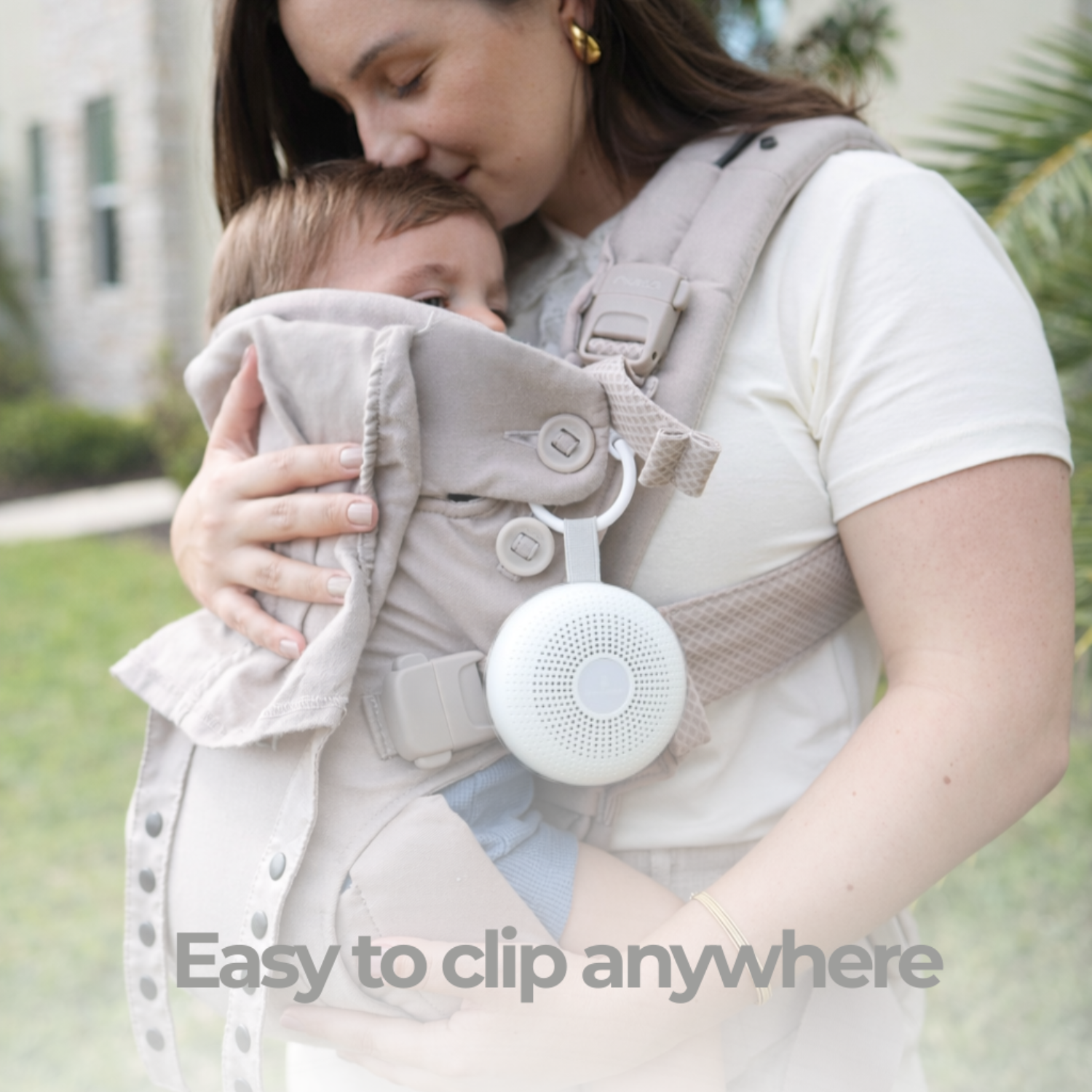 Woman holding a child in a carrier with a white portable sound machine attached, outdoors.