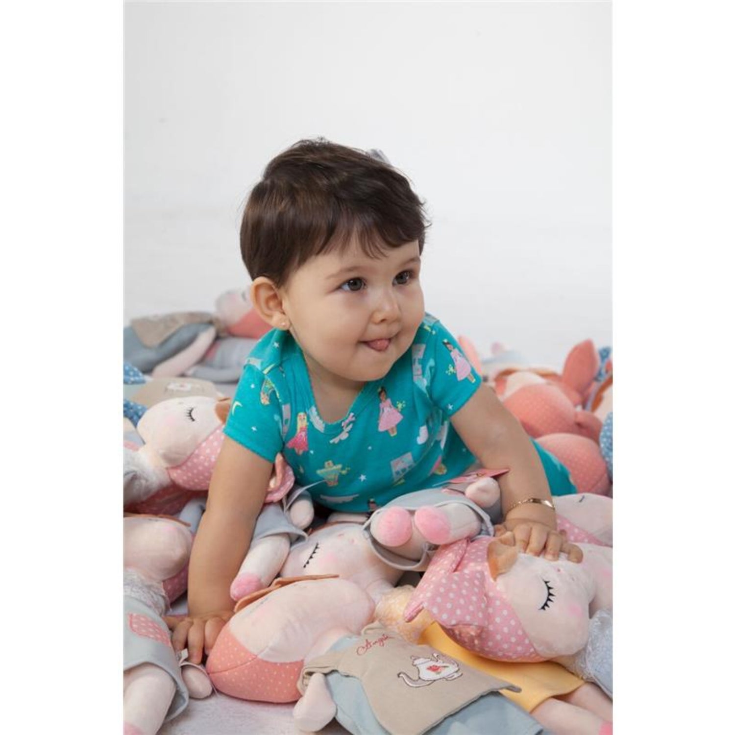 Toddler sitting on a pile of soft plush bunny dolls, smiling while playing. The cuddly dolls feature embroidered closed eyes, pink bunny ears, and pastel-colored outfits, creating a cozy and playful scene perfect for imaginative play and comforting snuggles.
